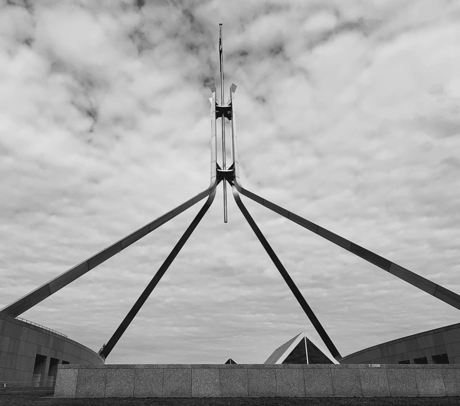 grey scale photo of the flag pole at the top of the Australian Parliament.