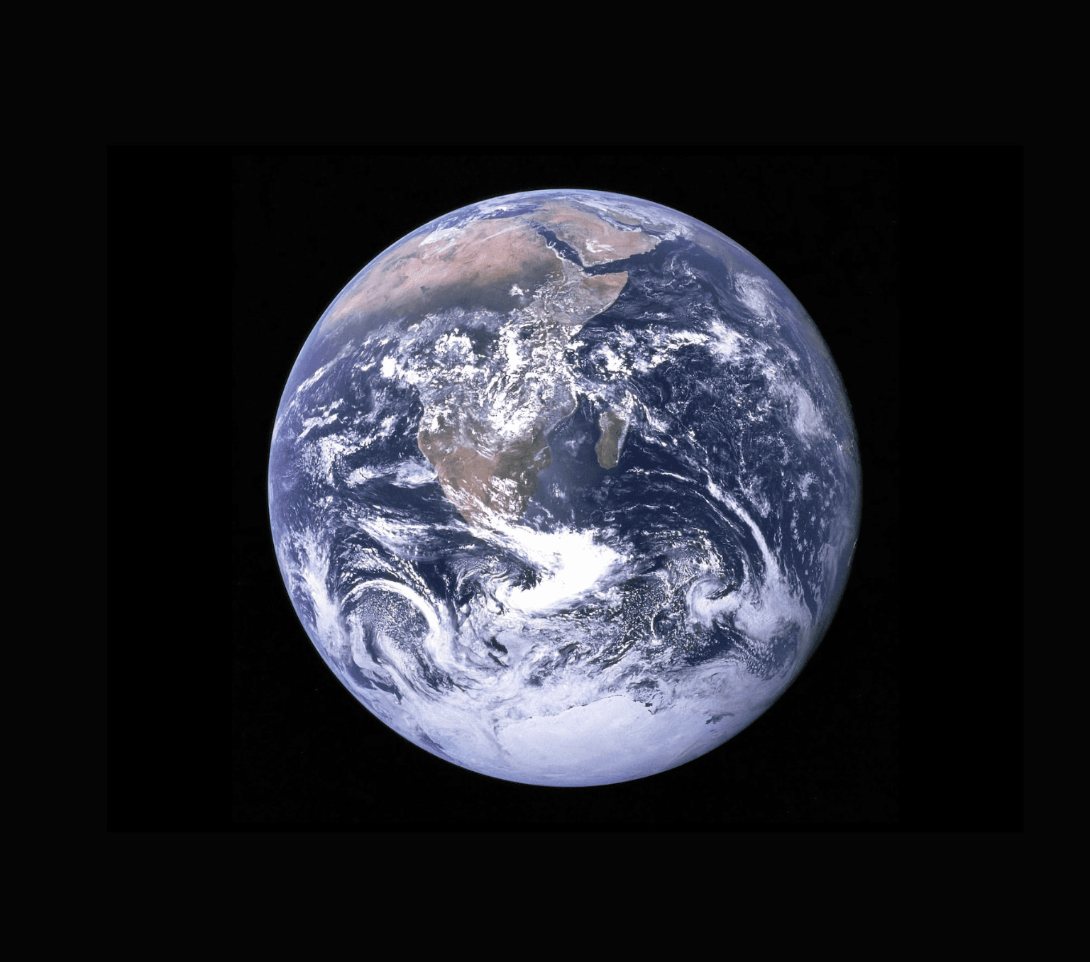 Earth viewed from space. Brown land and blue water and shown through white clouds. The background is black.