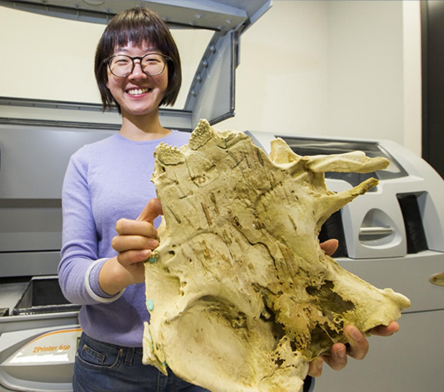 Yuzhi Hu smiles at the camera and holds a large fossil structure.