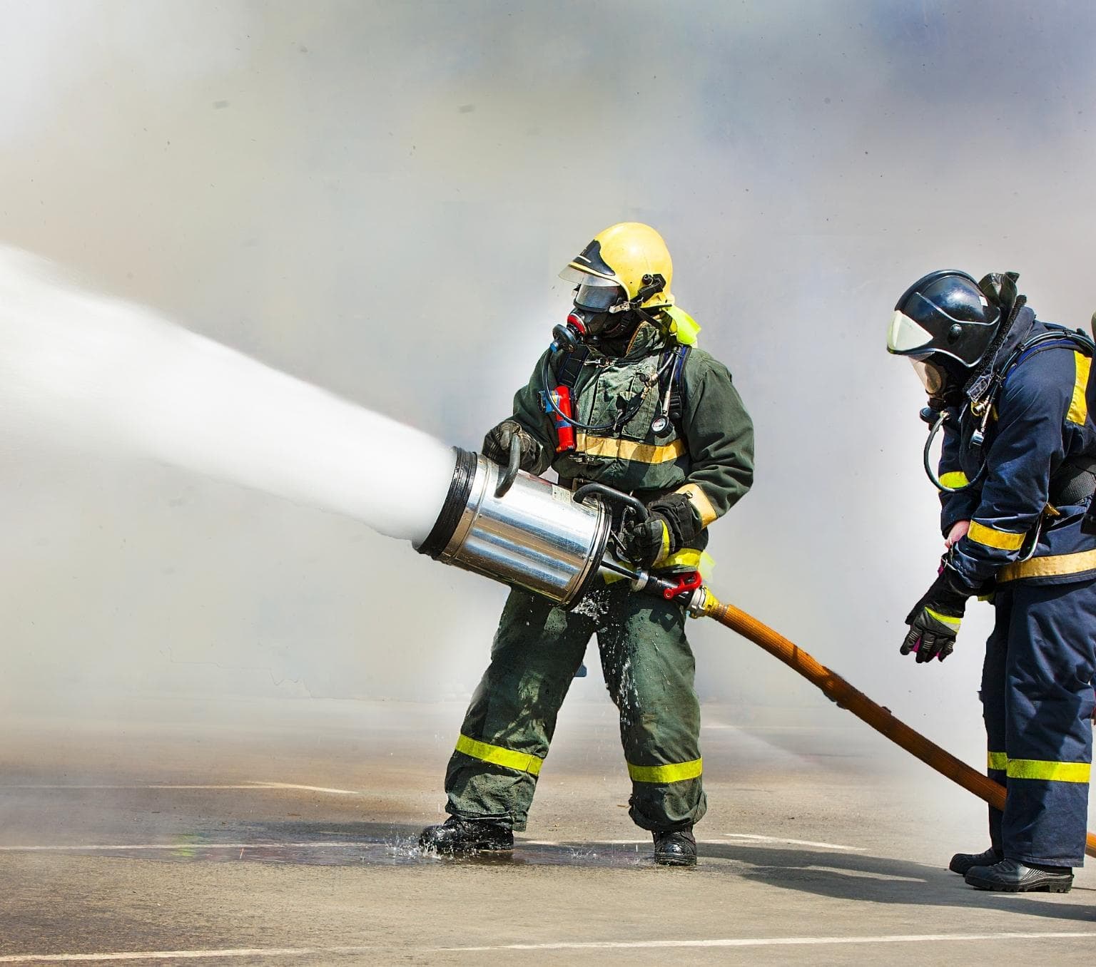 Two people wearing fire people suits. One is holding a large water gun that is spraying water.