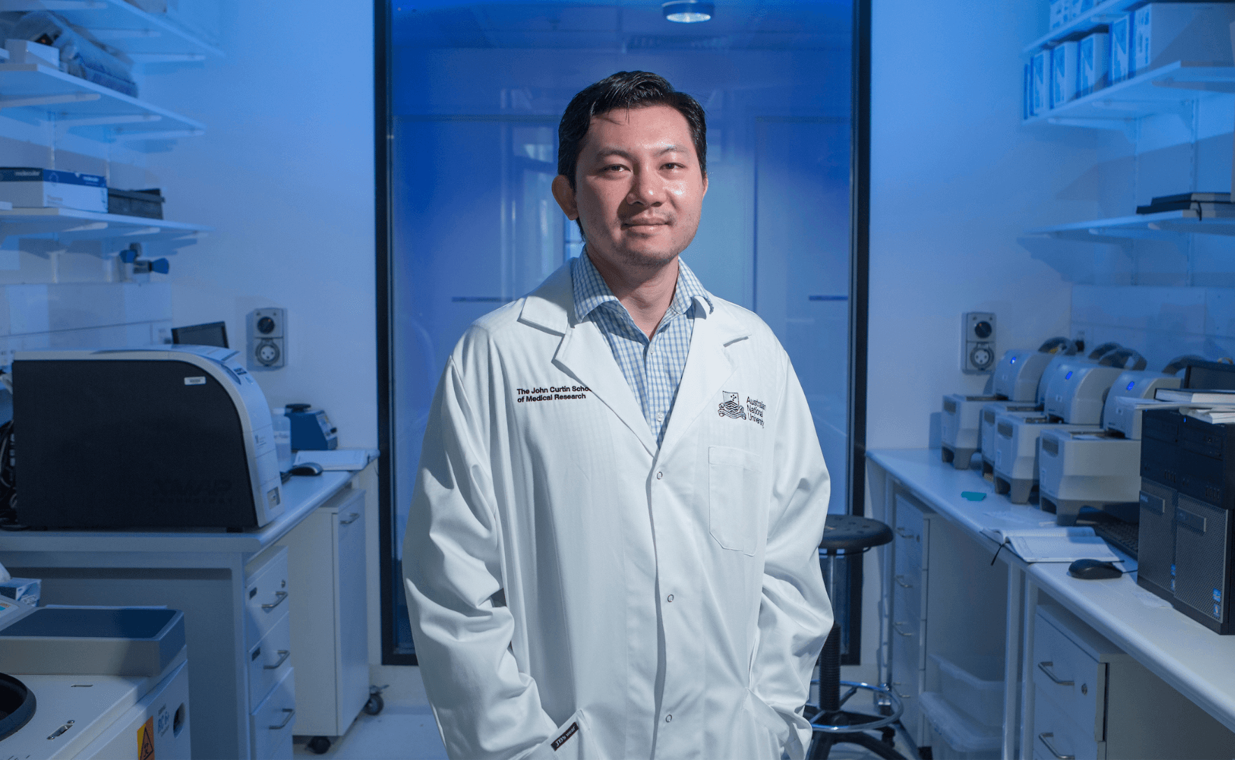 Professor Si Ming Man stands in an office wearing a white lab coat, with his hands in his pockets.
