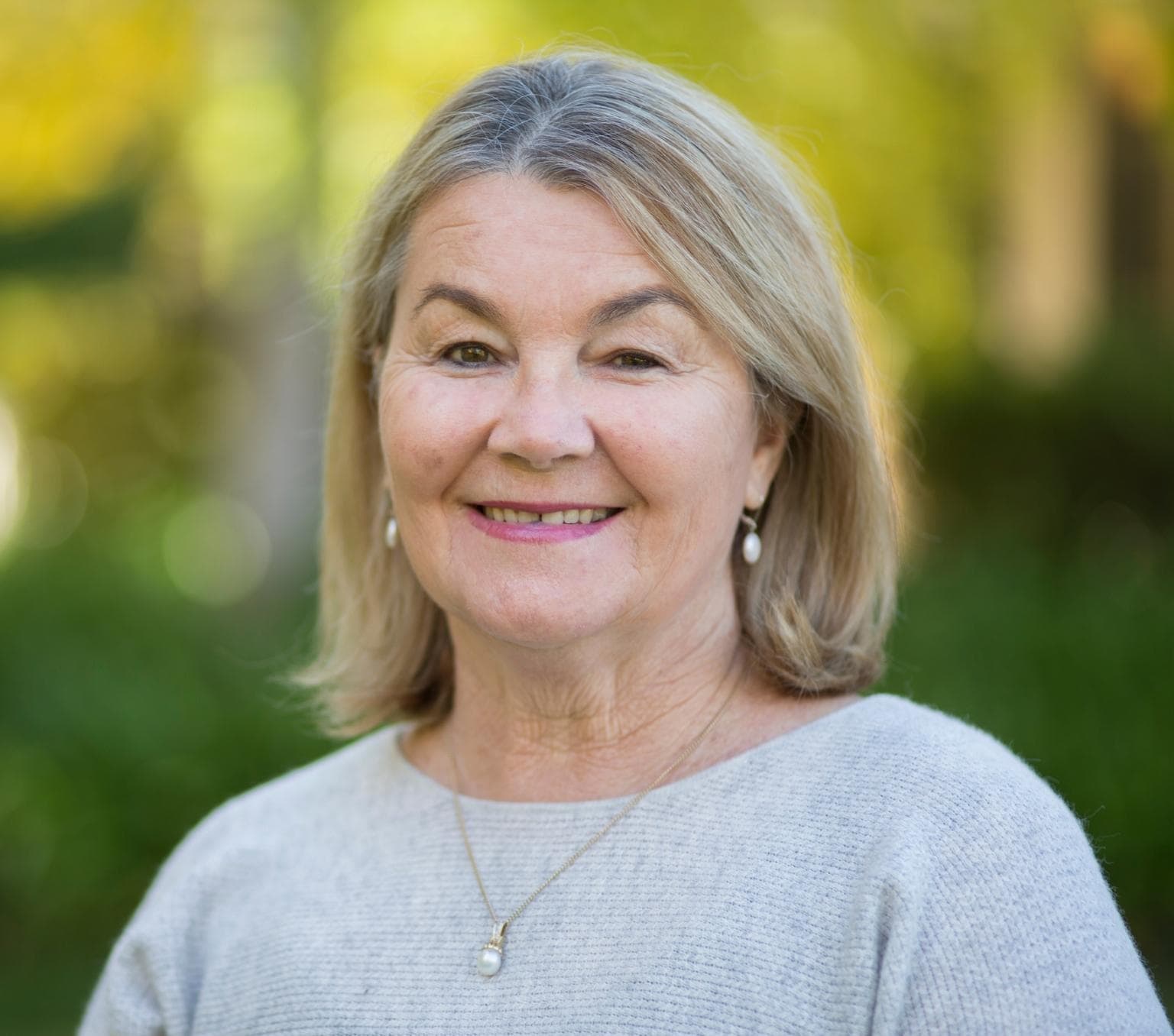 Photo of Ann from the chest up. She is wearing a light grey jumper and is smiling at the camera.