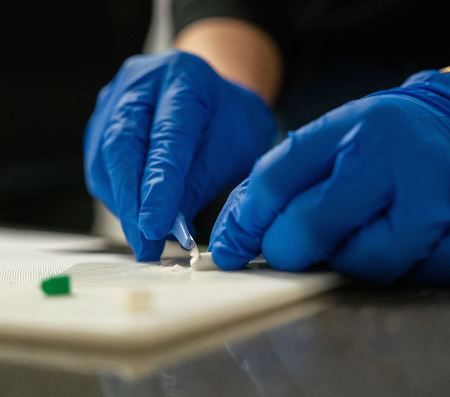 Hands in gloves cutting open a pill capsule