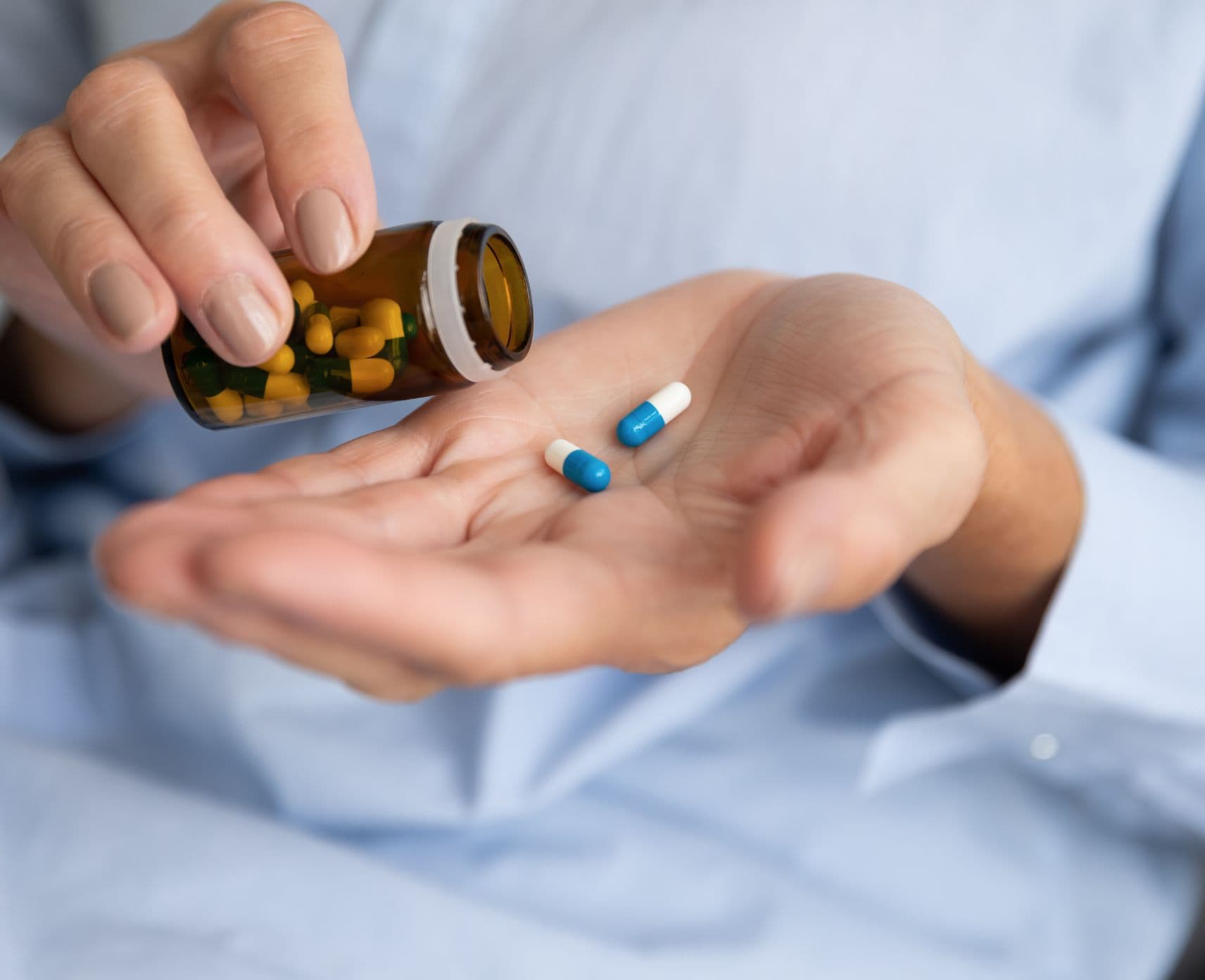 A close-up of a person with two pills in one hand. They are holding the pill bottle in the other.