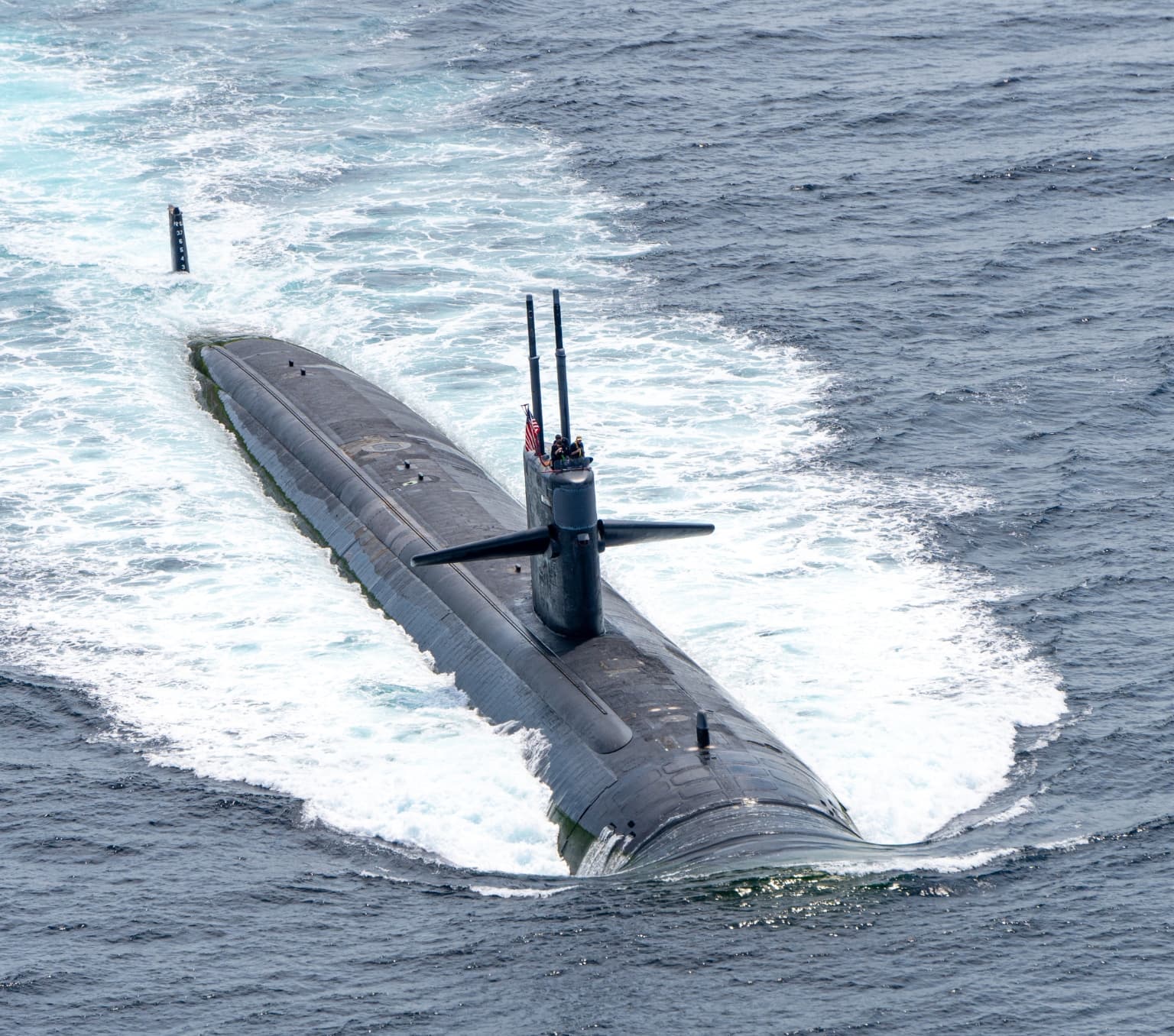 A submarine in the ocean. There is a US flag on top of the submarine.