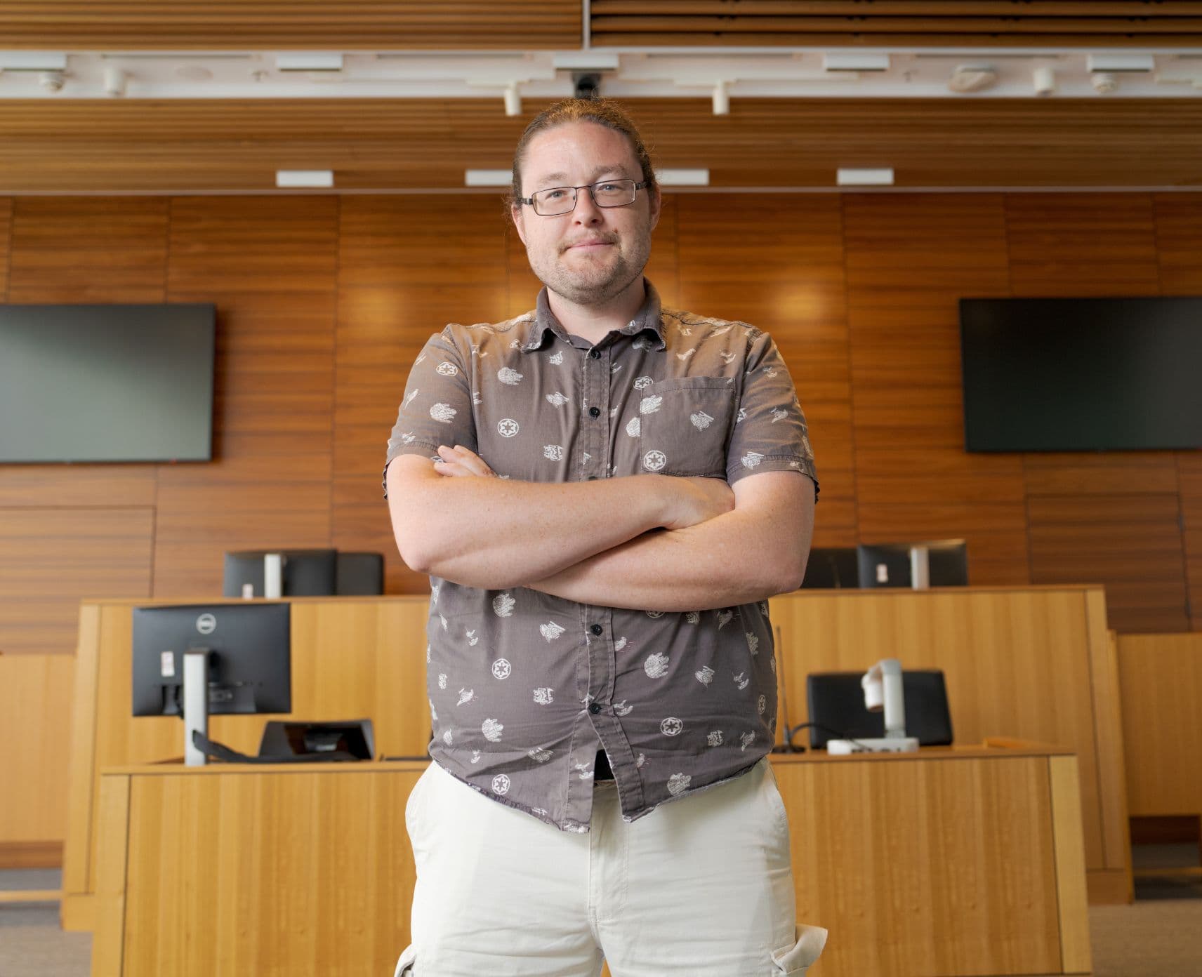 A man standing with his arms crossed in front of a wooden court room.