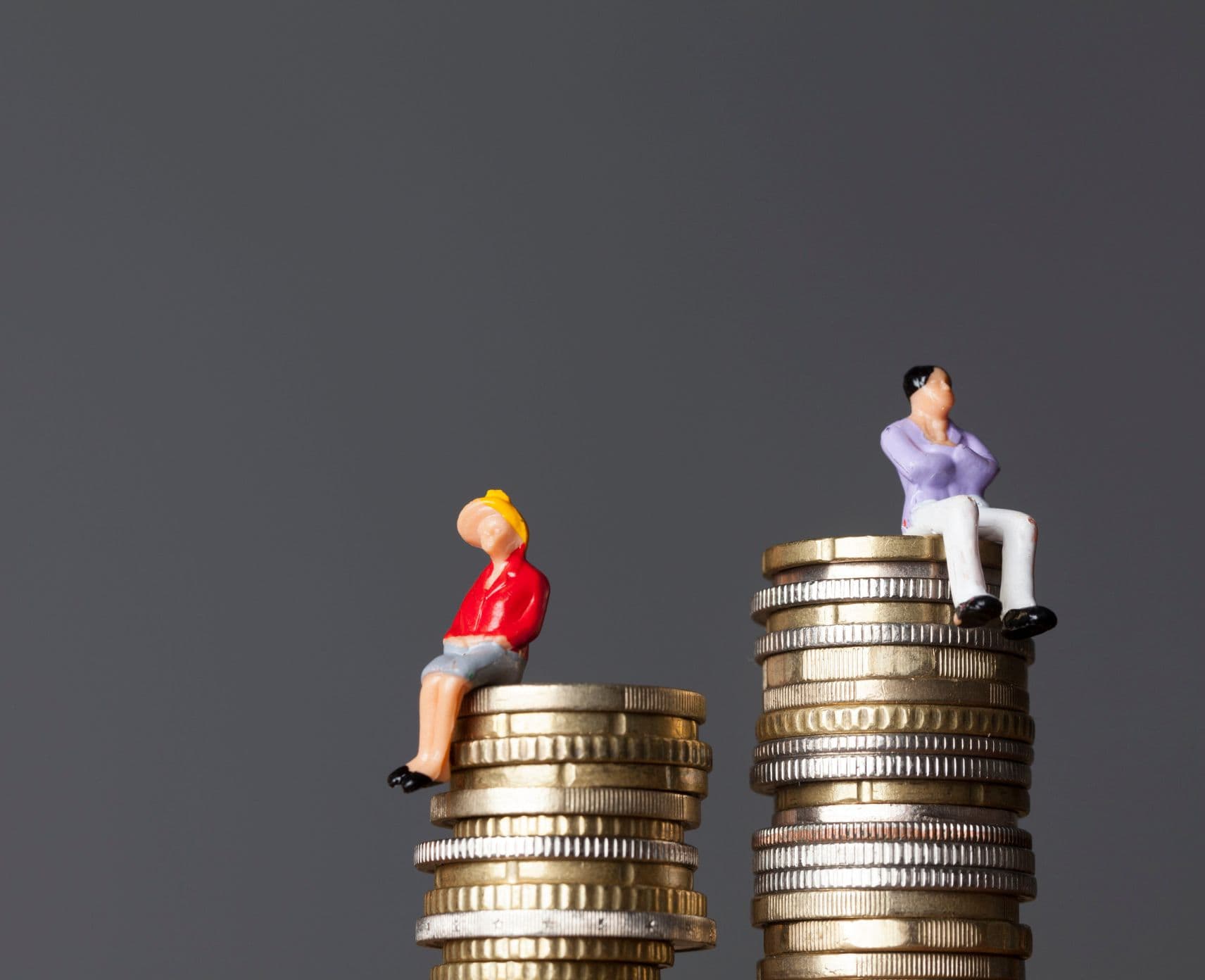 A male and female figurine sitting on two piles of coins. The male figurine is on a taller stack.