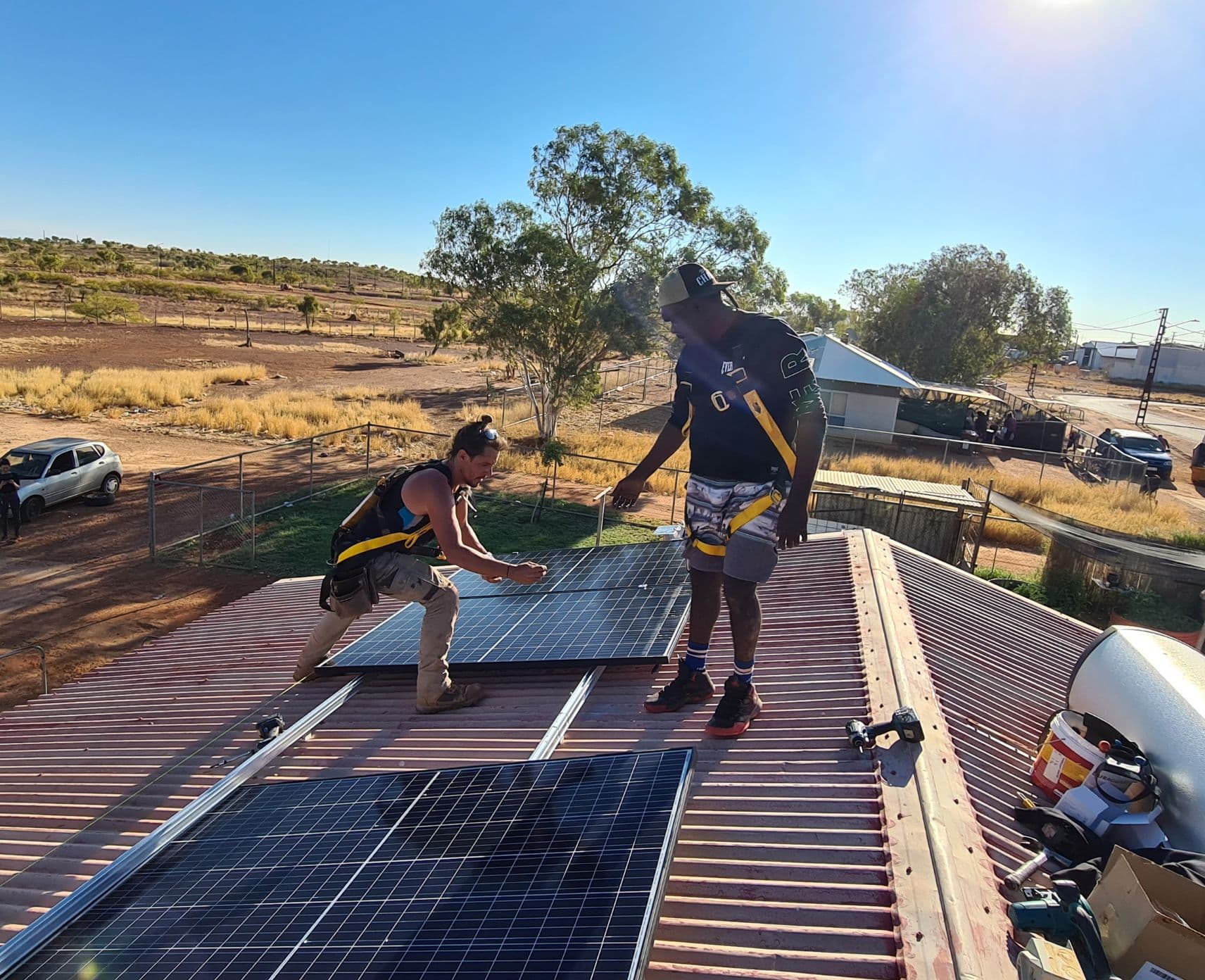 Two men stand on a roof with solar panels.