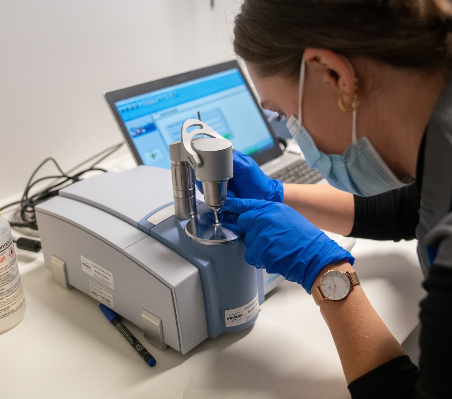 A CanTEST worker is examining a small scraping of an unknown white powder using advanced machinery. You can only see the back of the worker's head.