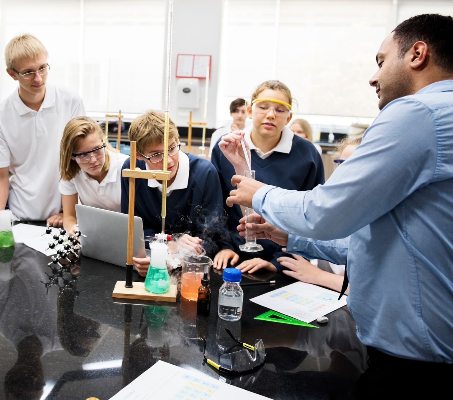 young school students looking at their teacher who is performing a science experiment