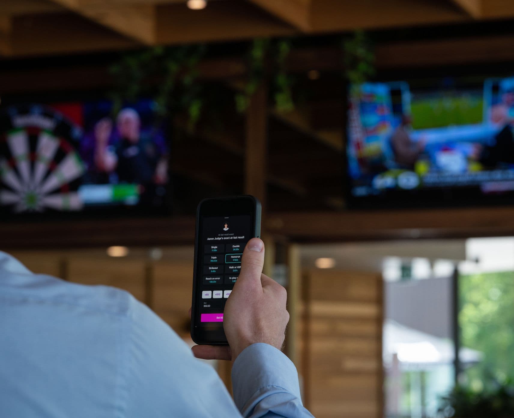 A young man holds up a mobile phone while watching a sporting match on TV.