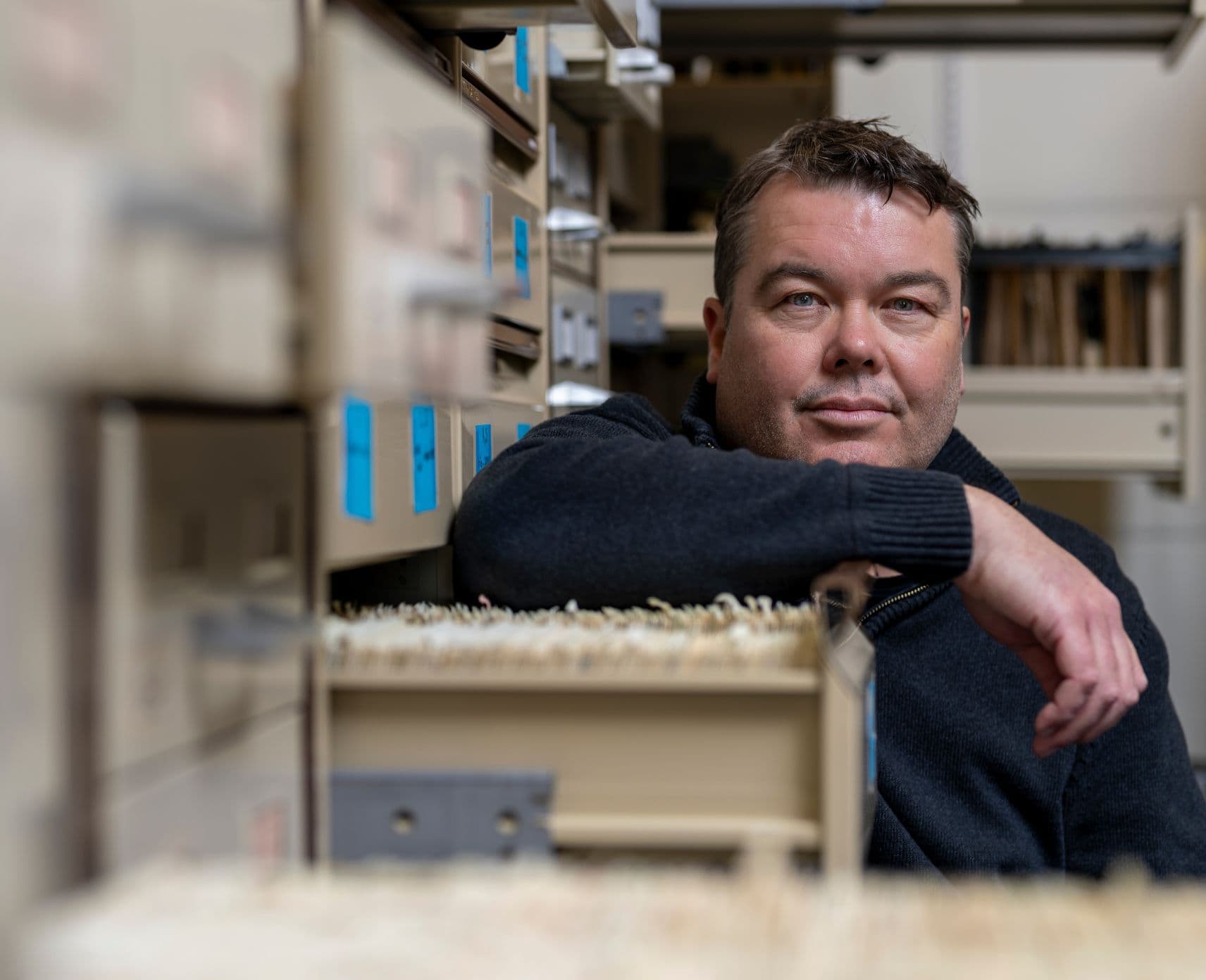 a close-up of Mark looking at the camera and resting his arm on a filing cabinet