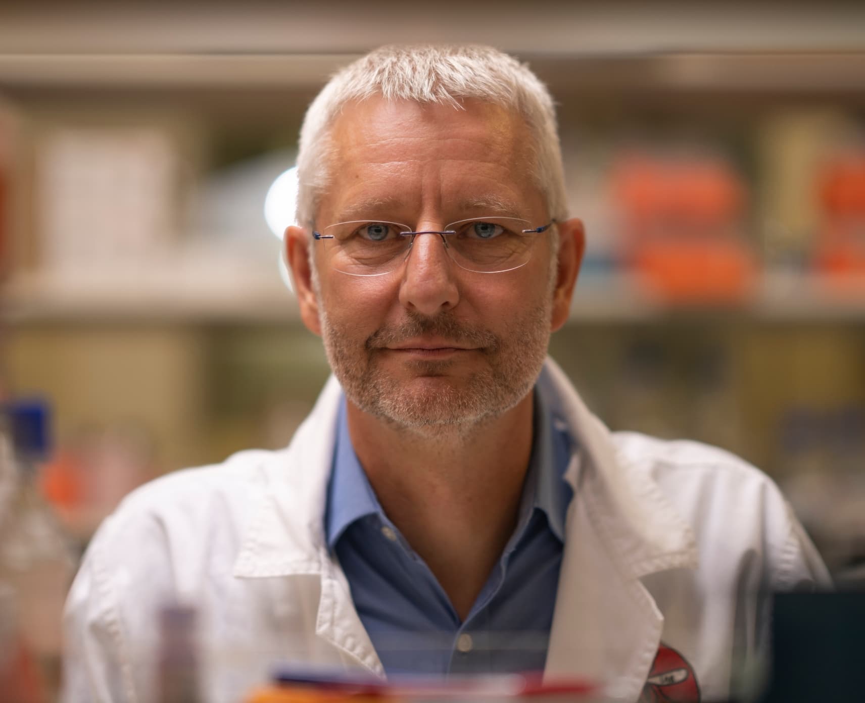 Professor Alex Maier is wearing a white science lab coat with a blue collar shirt underneath