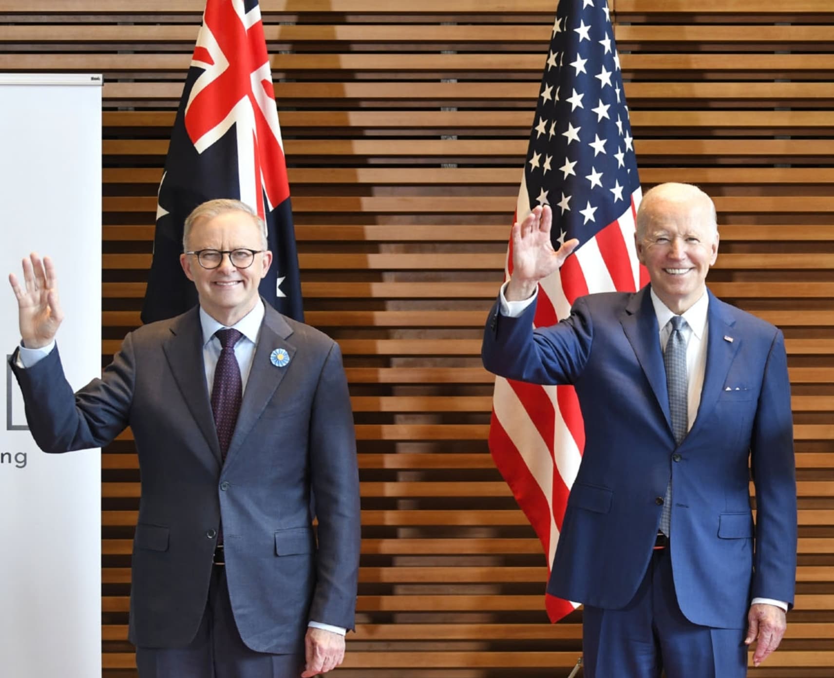 PM Anthony Albanese and President Joe Bident smile and wave in front of respective flags. The odd couple