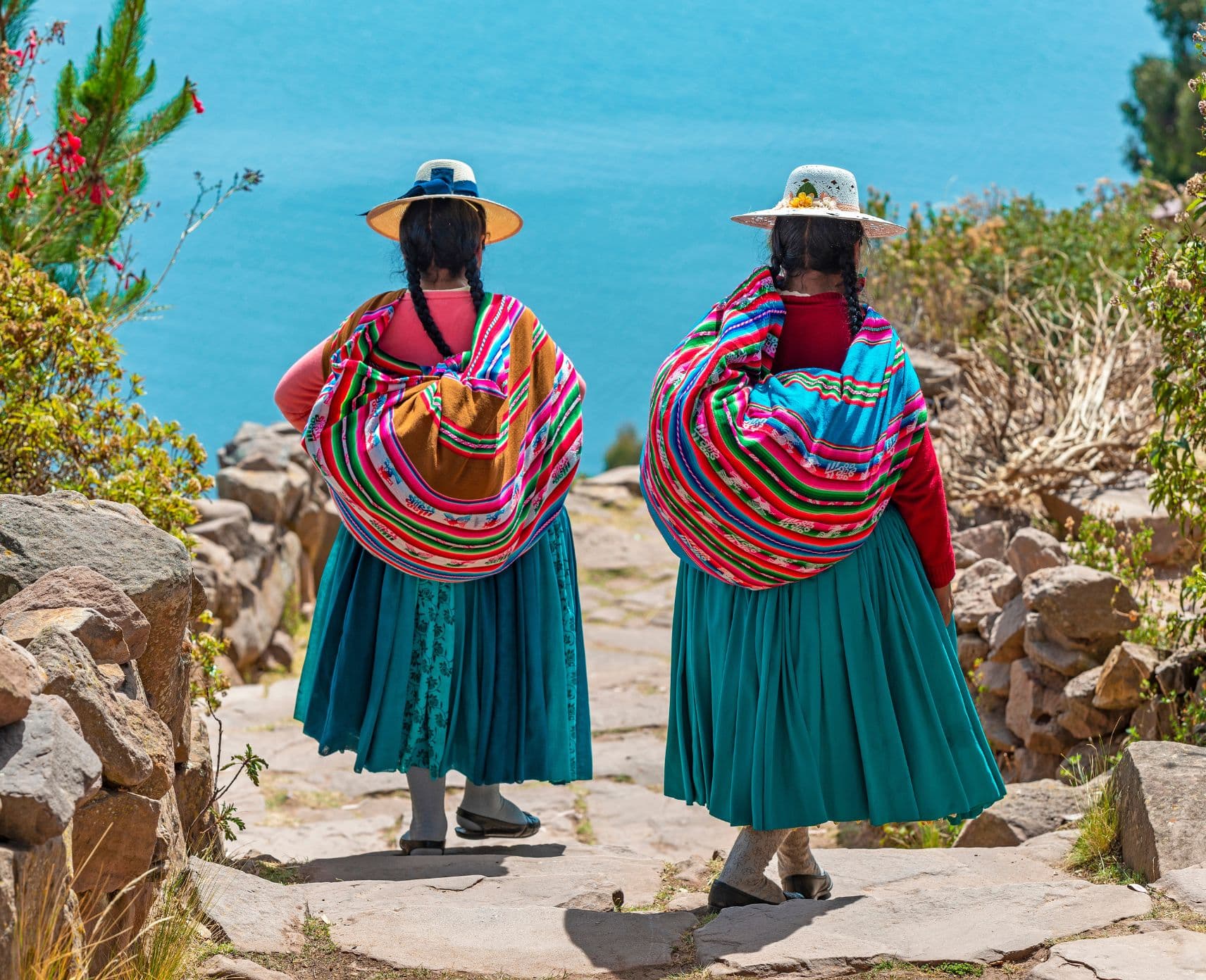 The backs of two women in traditional costume walking to the beach.