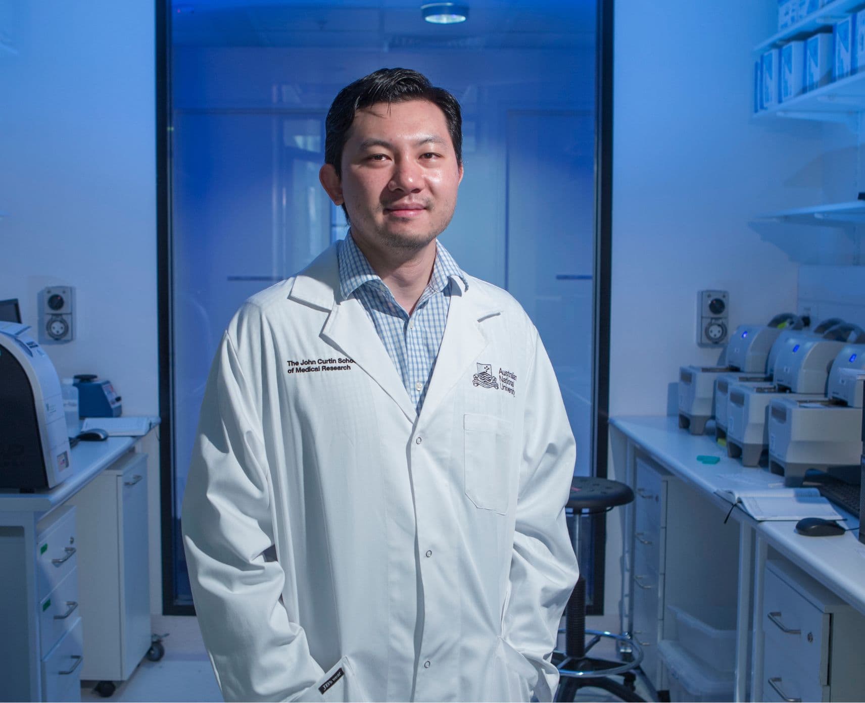 An ANU scientist standing in a lab in a lab coat.