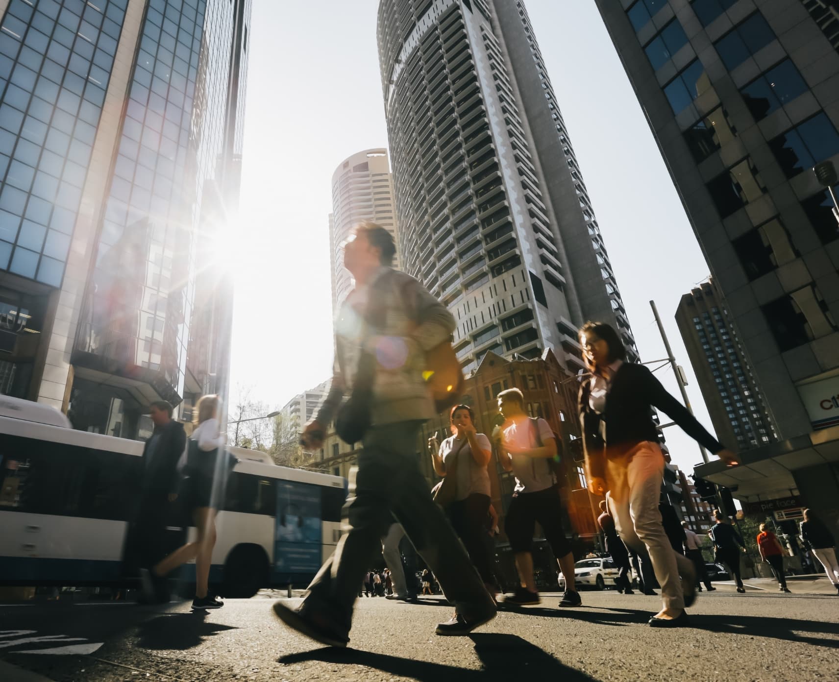 Pedestrians on a street in Sydney CBD. Light beams down from skyscrapers