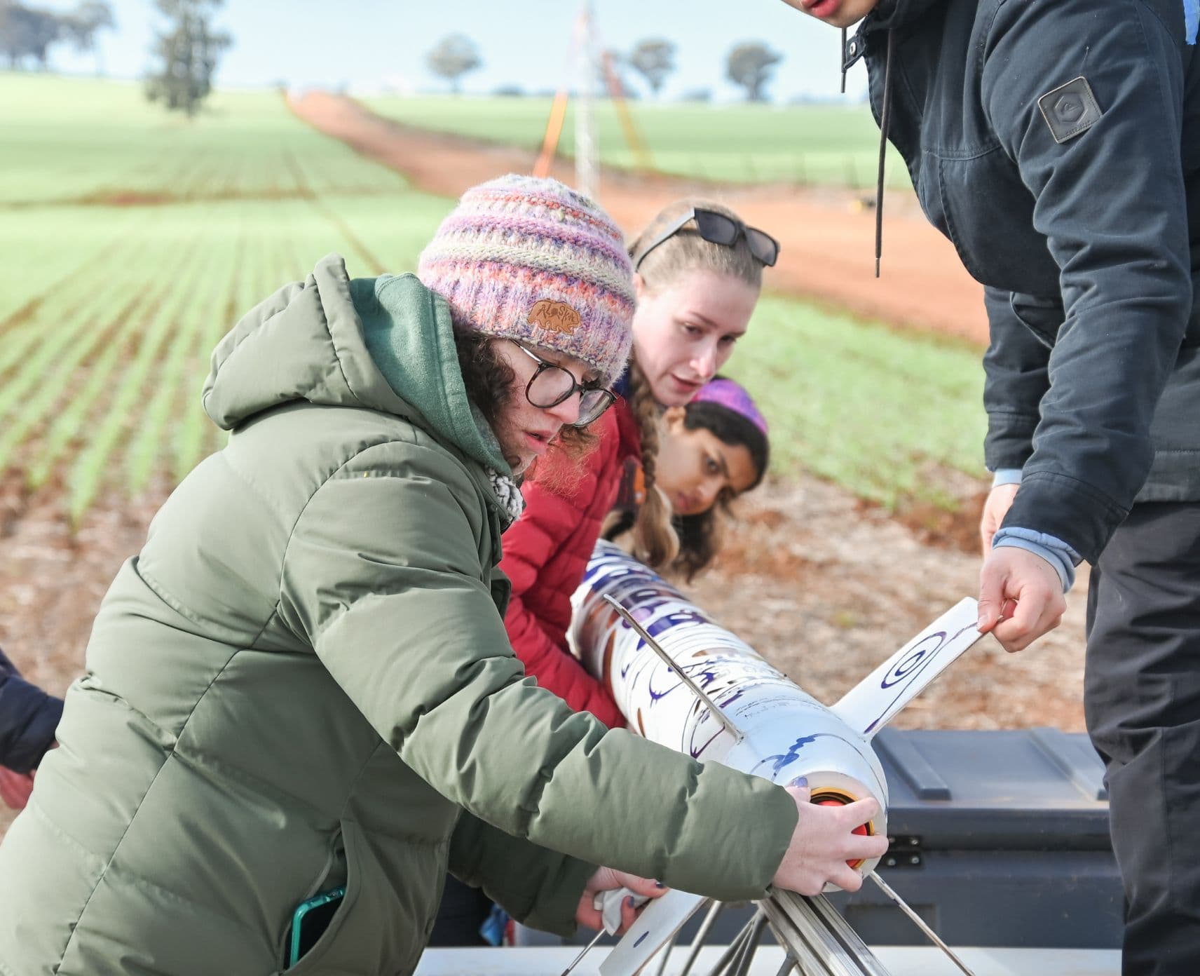 Four people assembling a rocket together in a field.