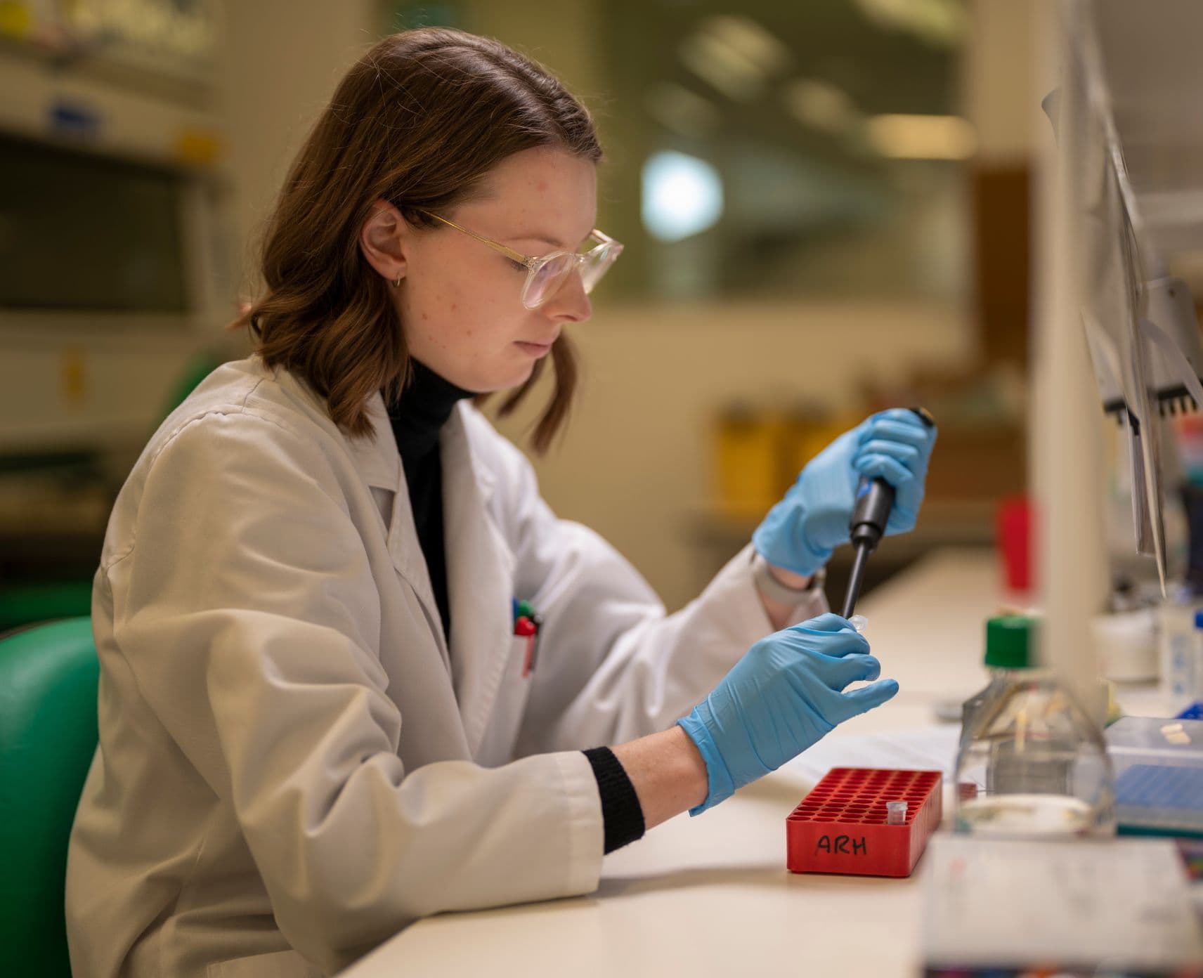 Close up of Dr Samantha McGaughey in the lab. She's wearing a white coat and blue gloves.