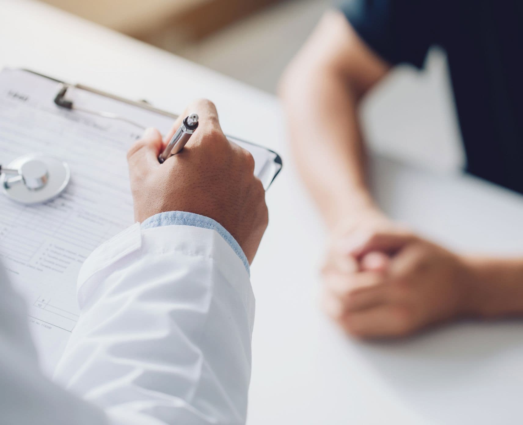 Hand of a doctor in a white lab coat writes notes during consultation