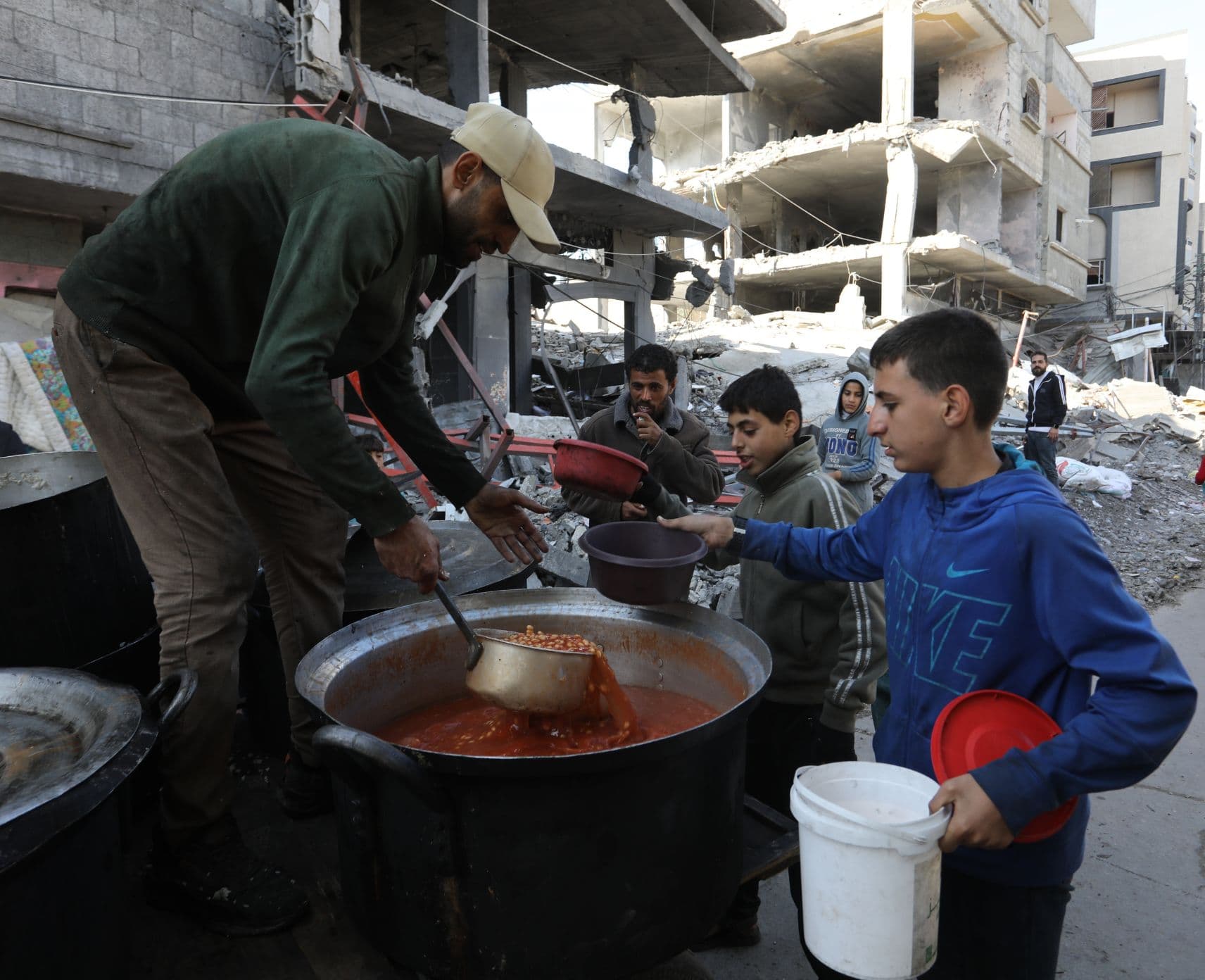 A man hands out food to people, surrounded by destroyed buildings.