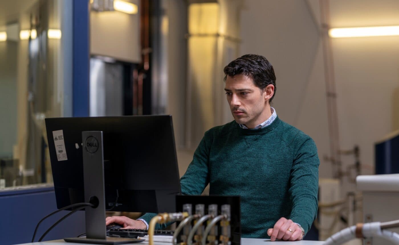 ANU Professor Nicholas Chilton (pictured) is sat at a desk looking at a computer. He is wearing a green sweater.