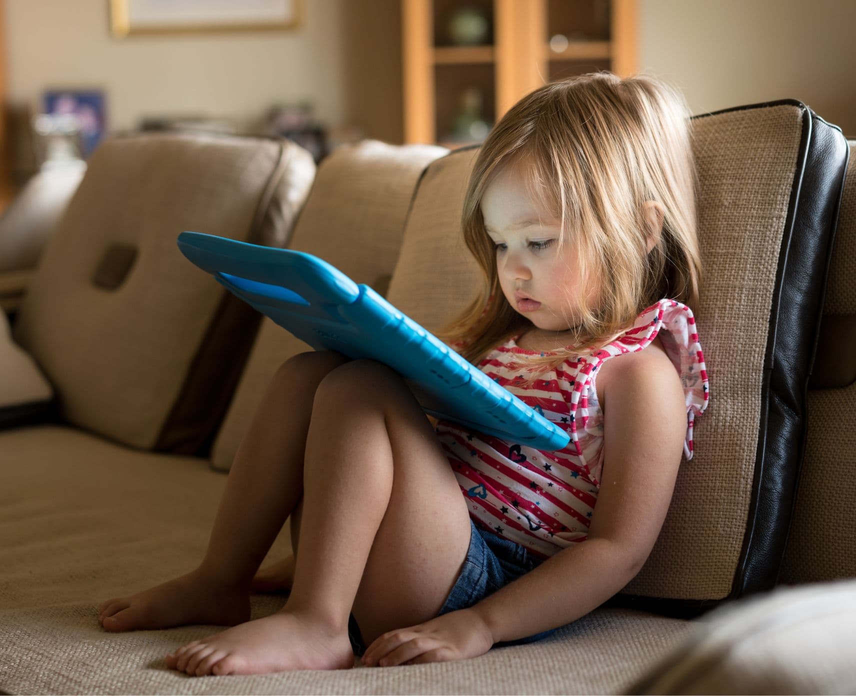 Child with an ipad sits on a couch