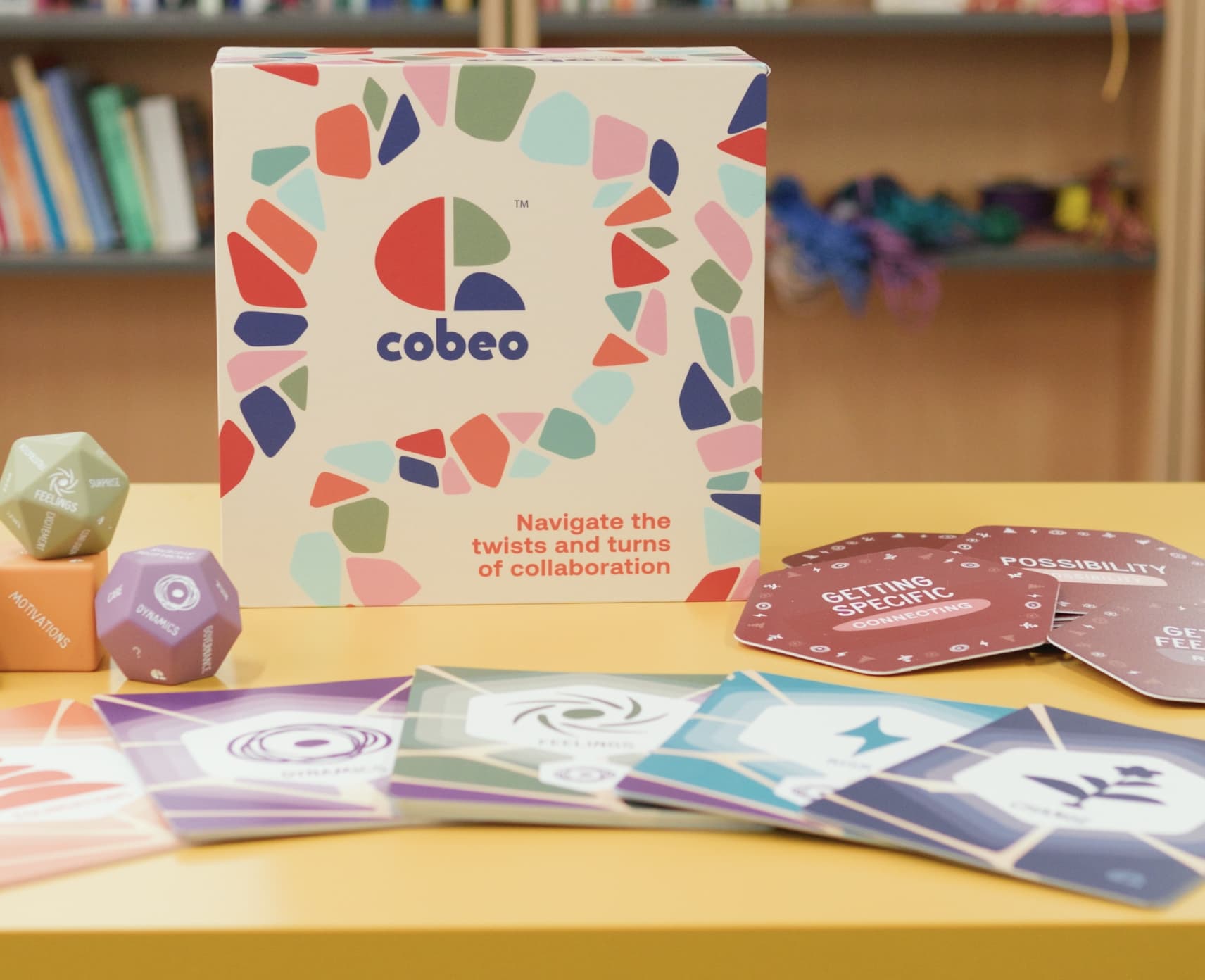 A box with the word 'Cobeo' on it. There are cards laying on a table in the foreground.