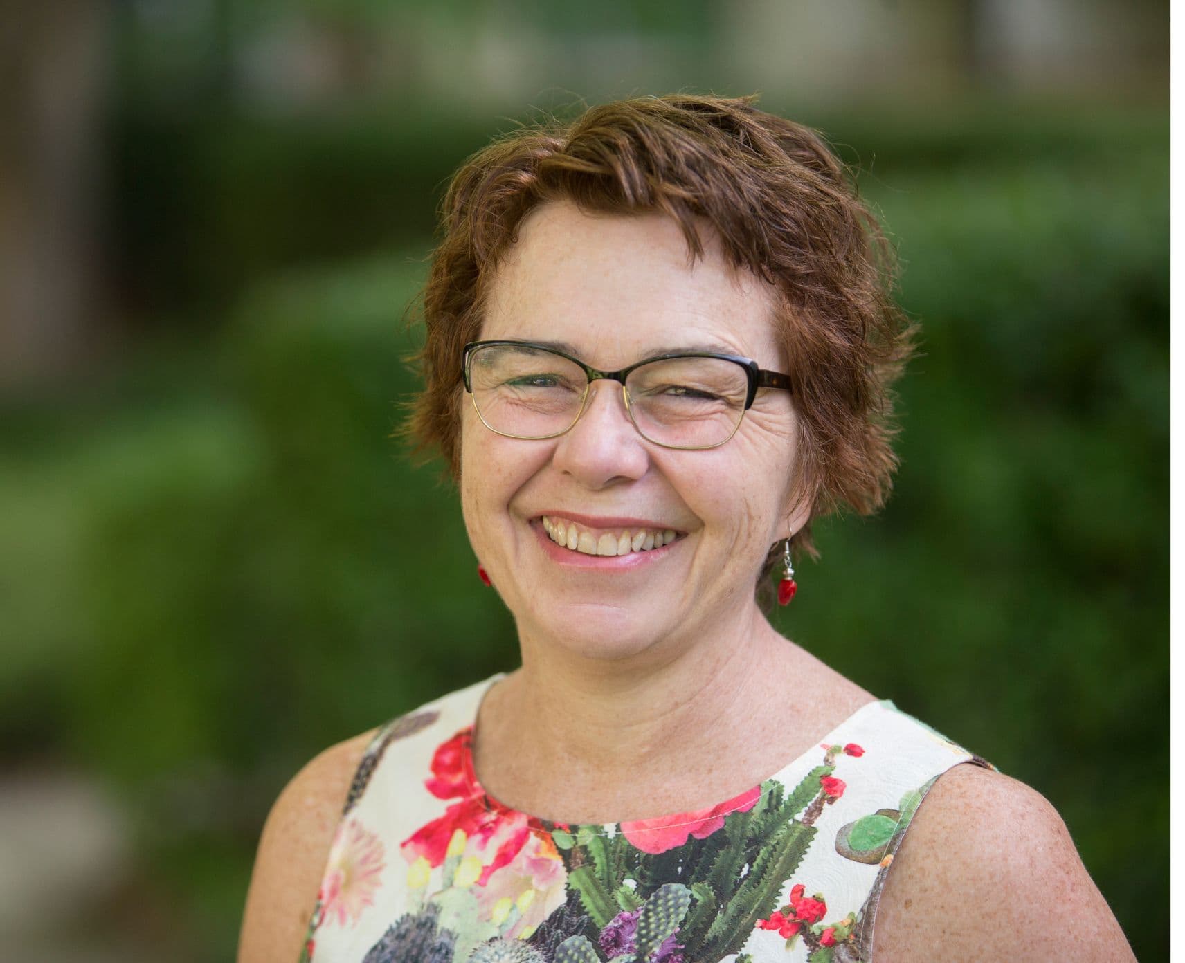 A woman standing in a garden smiles at the camera.