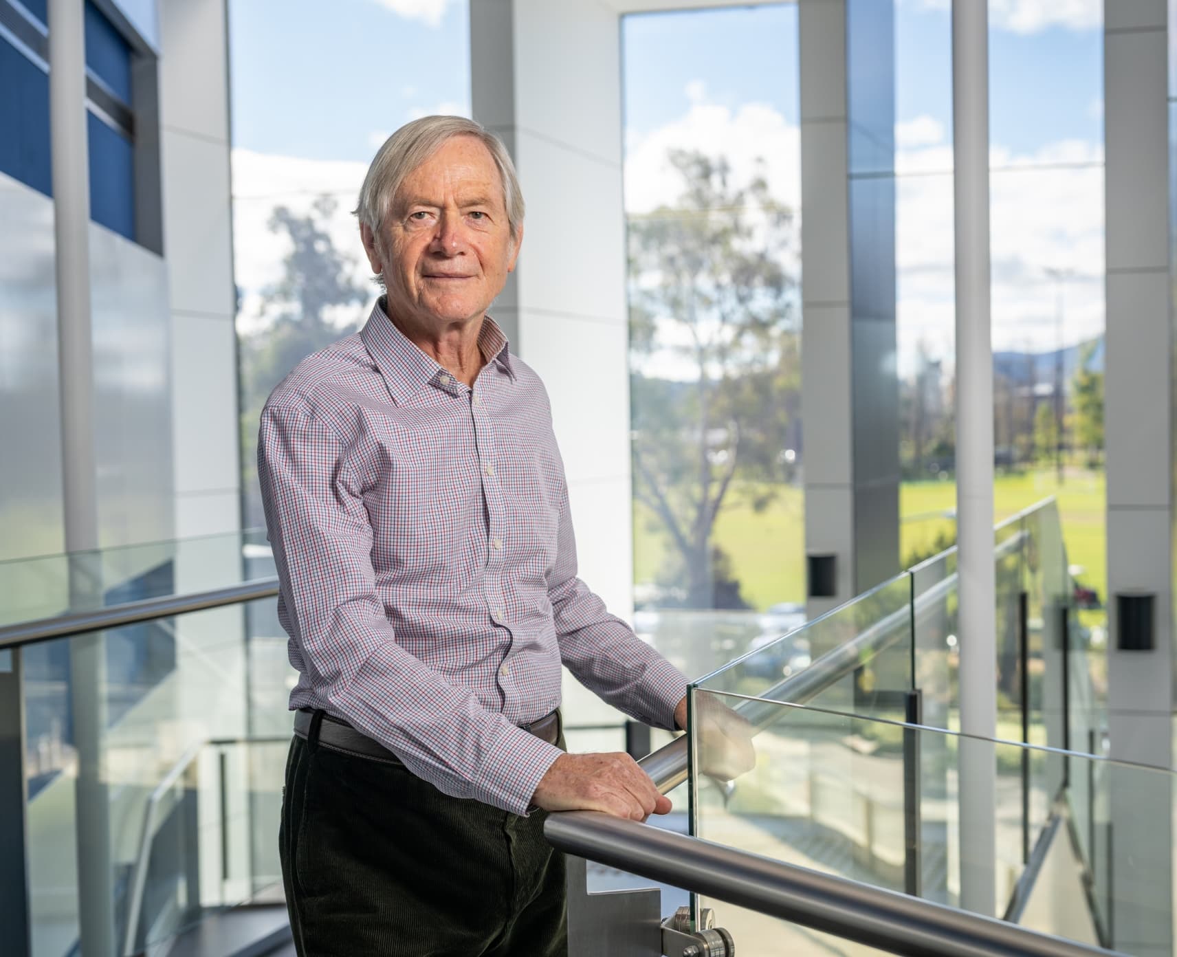 Trevor Lamb stands on an indoor walkway, in front of windows, through which a garden is visible.