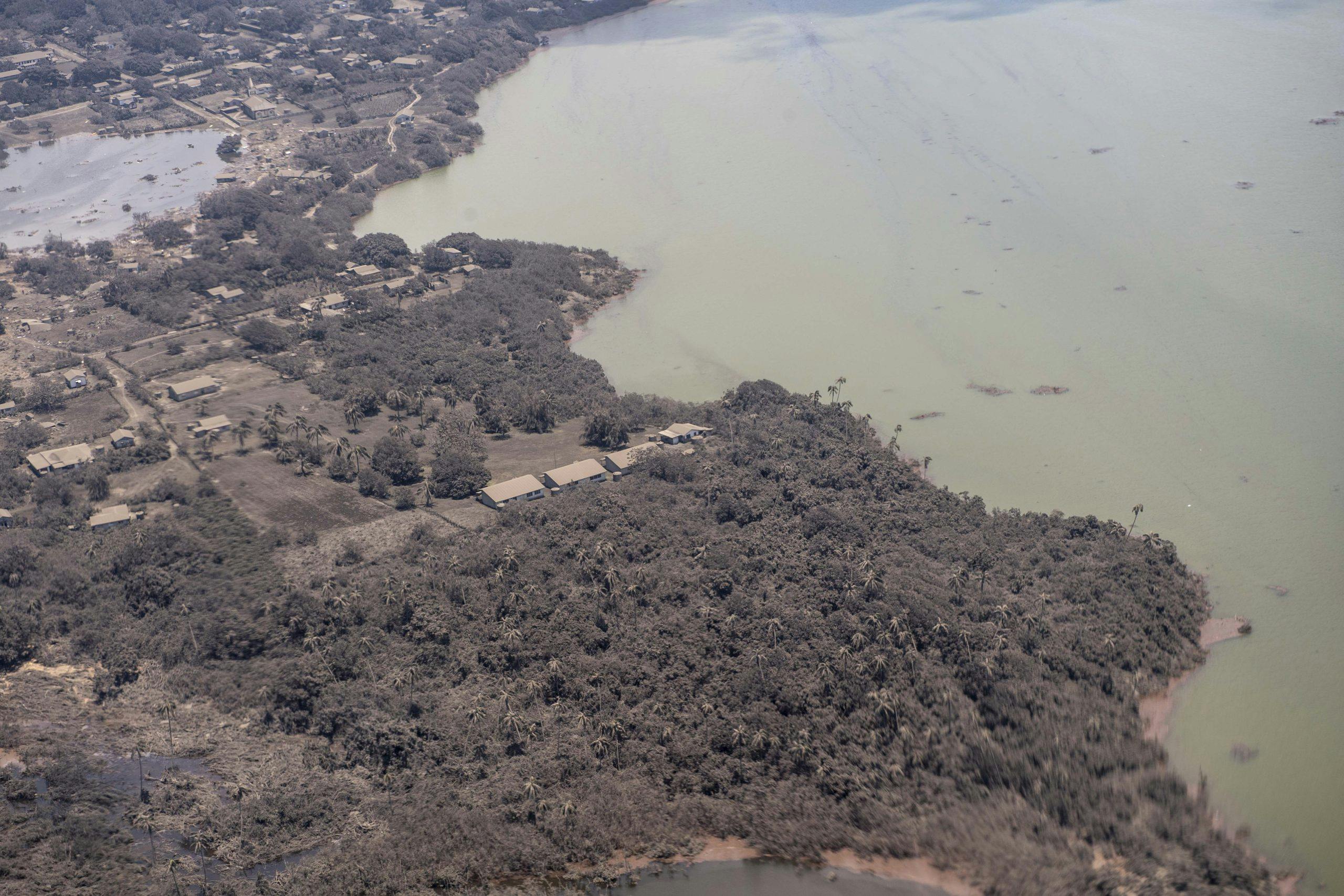 aerial view of bushland with some building scattered on the land and a coast of green water