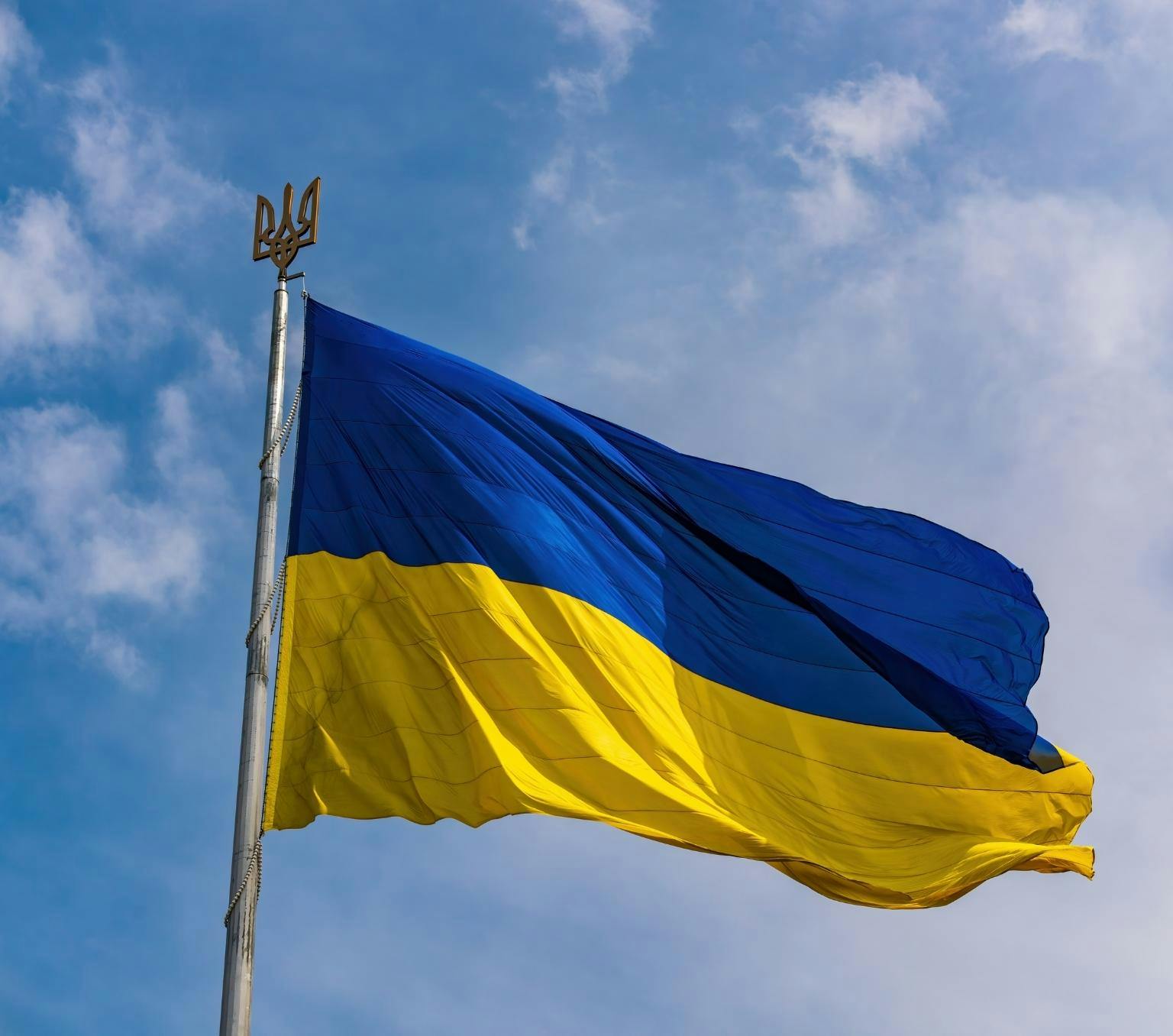 Ukraine flag flying on a mast in the sky. The flag is blue on the top and yellow on the bottom