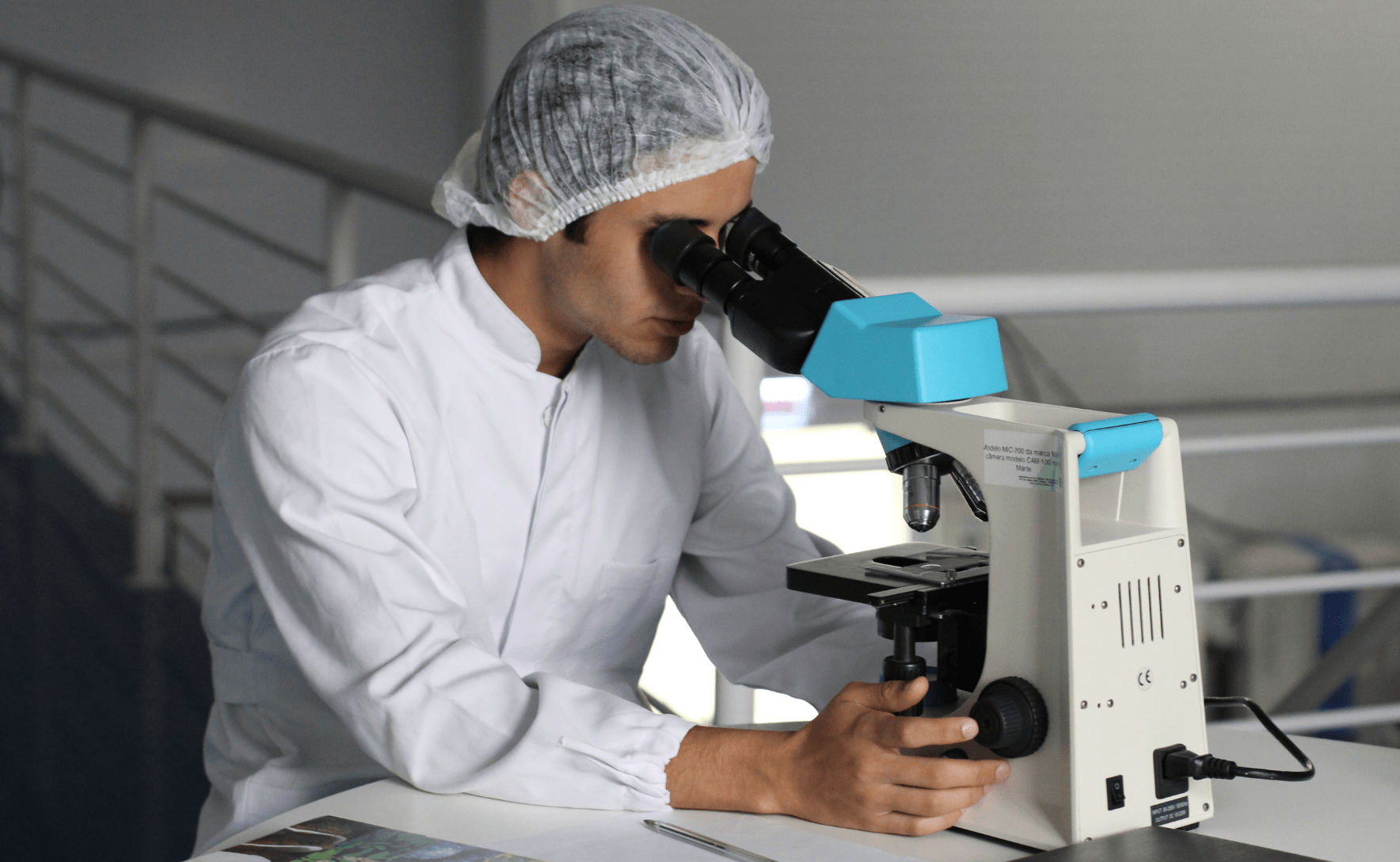 A man in a white lab coat is peering through a microscope.