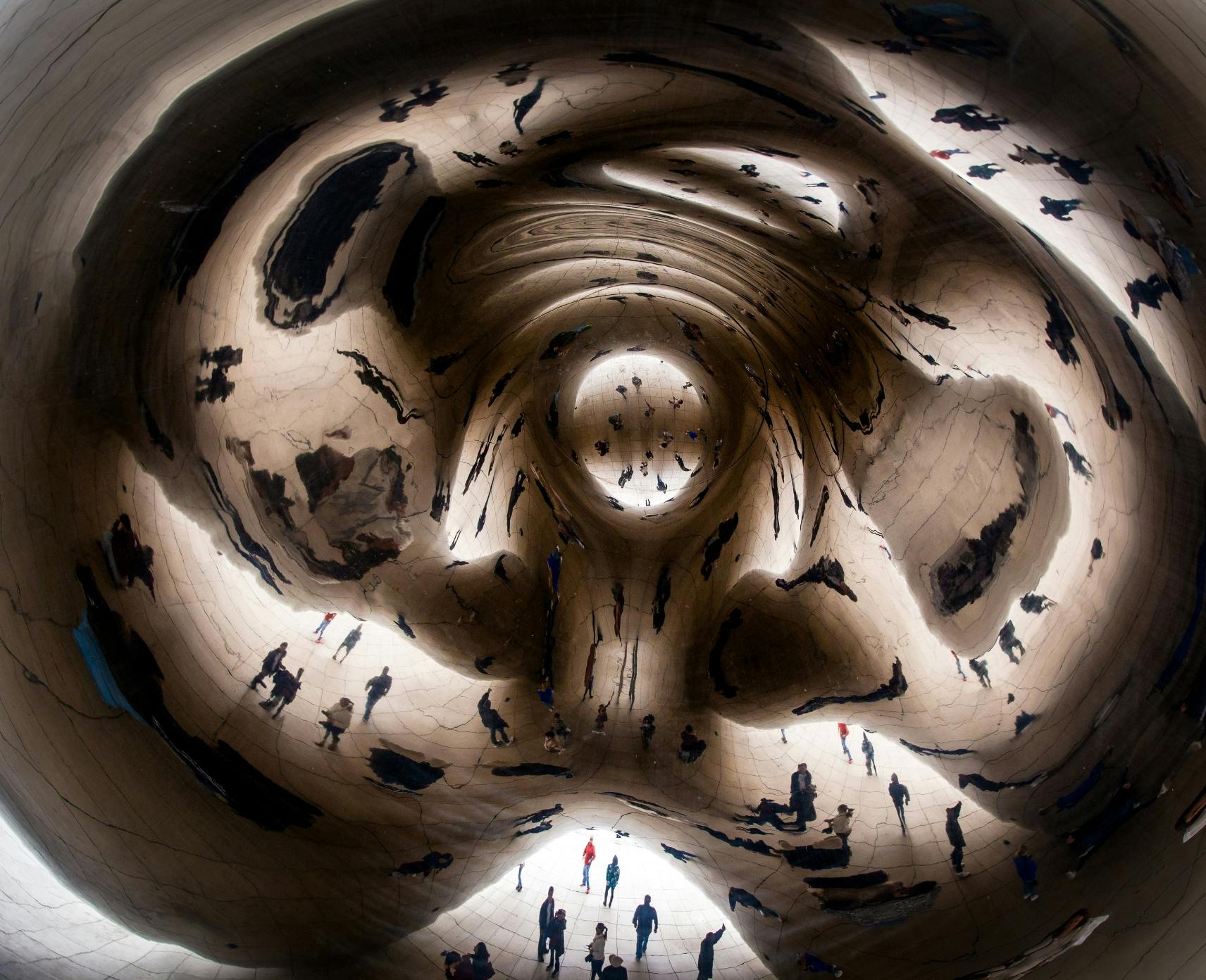 Distorted reflections of people in the Chicago Bean monument.