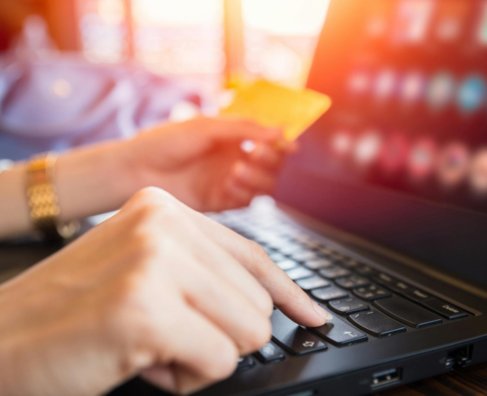 A person holds their credit card in front of a laptop