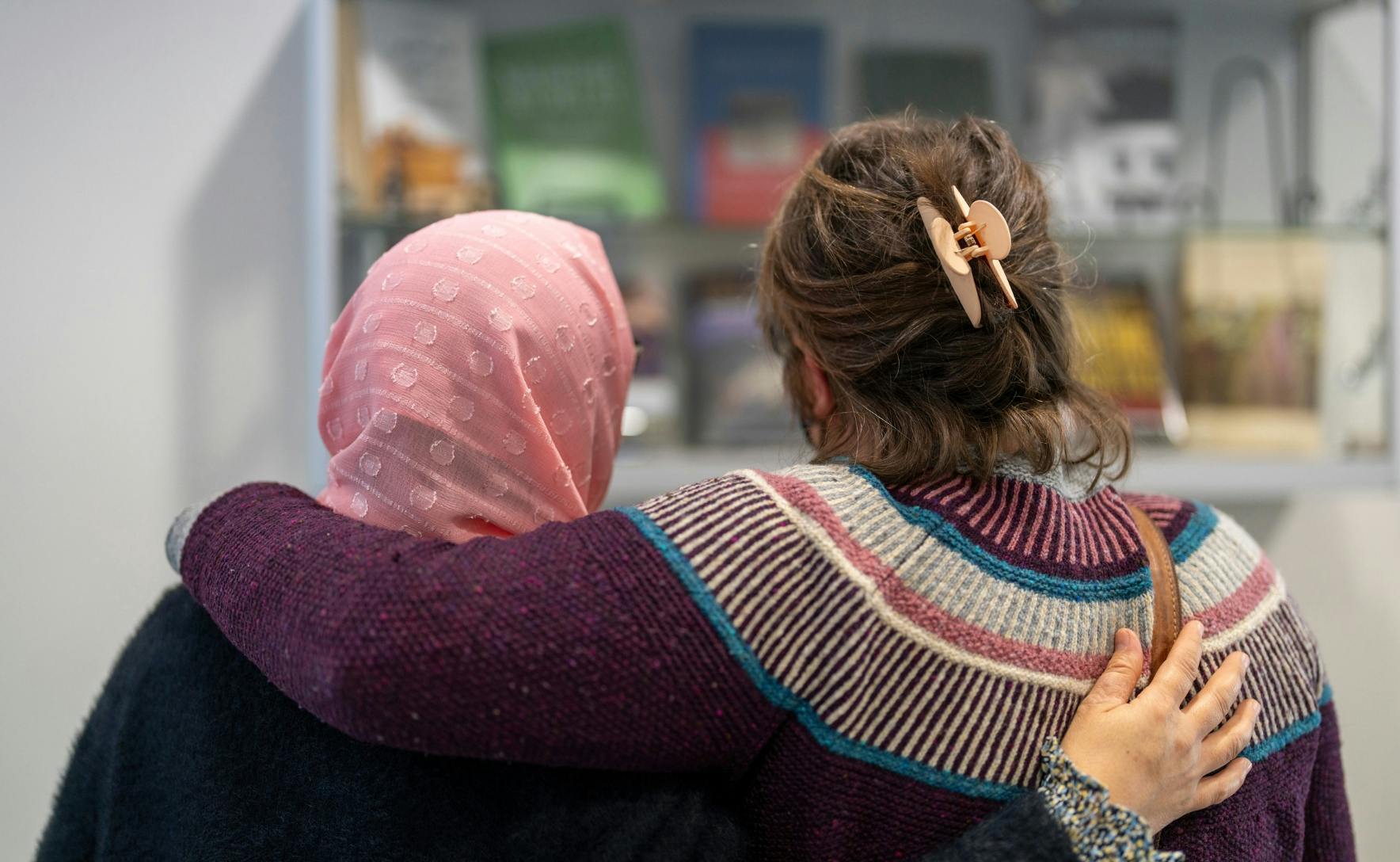 Susan and Soraya have arms around each other as they look at a display case of books