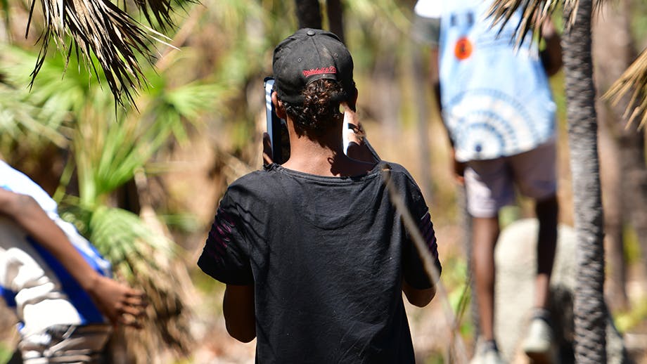 the back of a male teenager wearing a black shirt and black cap surrounded by bush