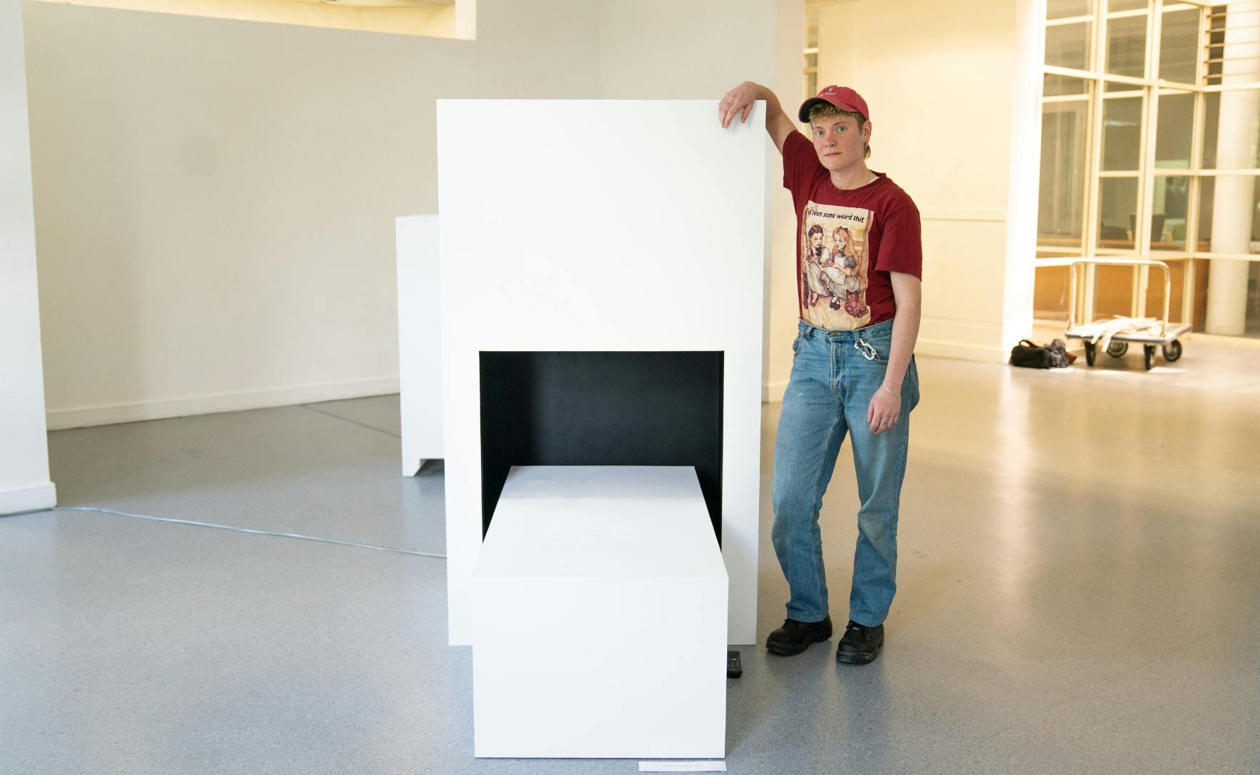 a person in a red shirt is standing with their arm resting on a white box and look away from the camera
