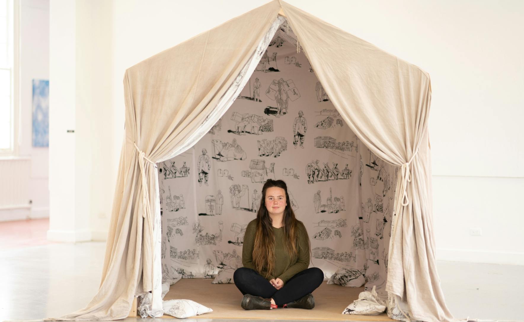 woman is sitting cross legged inside a large canvas tent