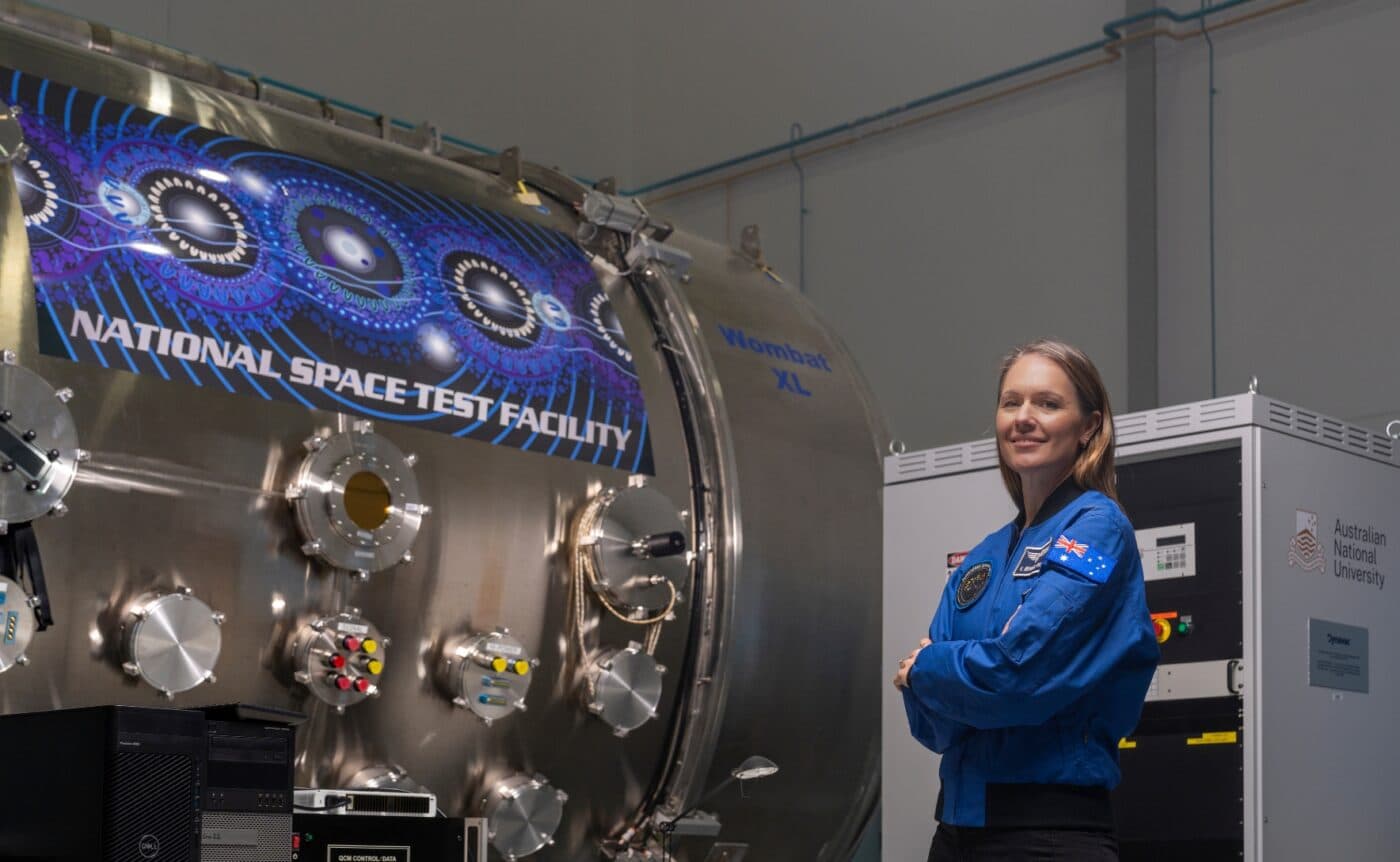 Katherine Bennell-Pegg with her arms crossed standing next to the National Space Test Facility device.