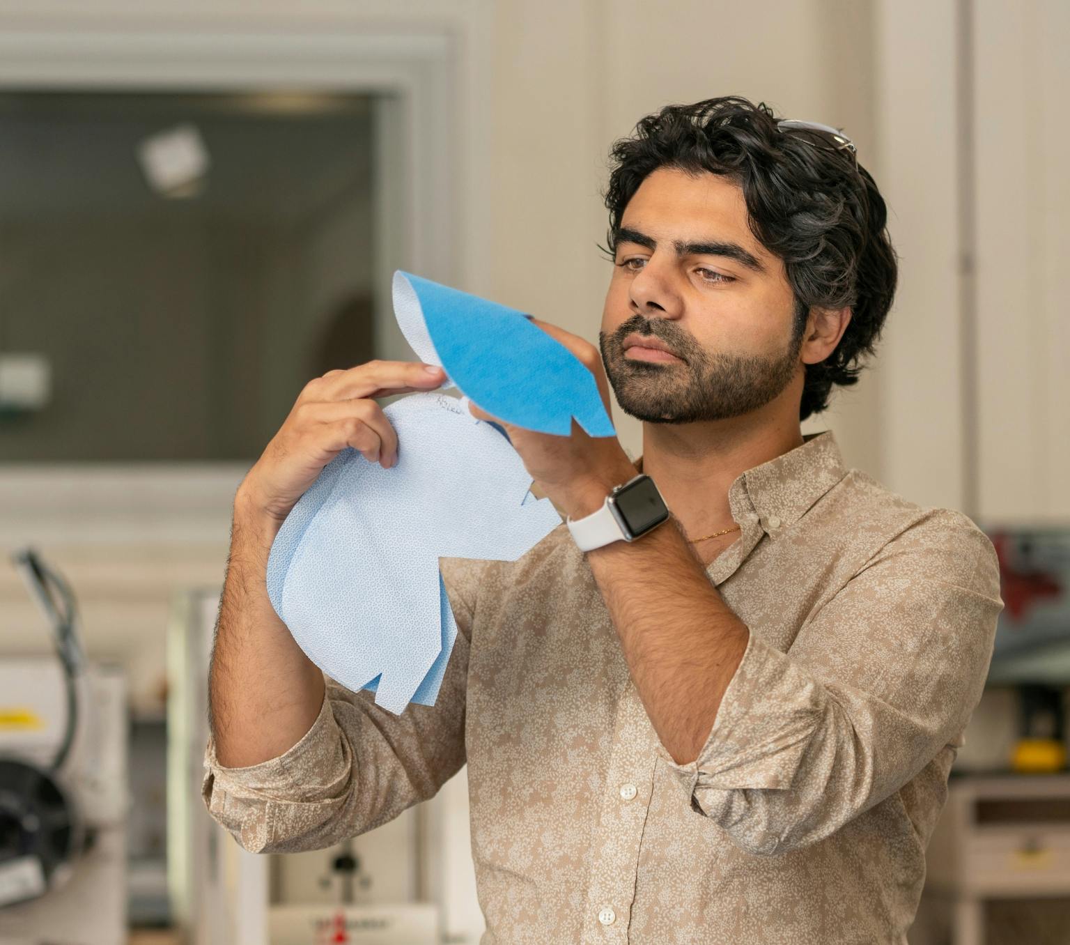 a man is holding up and looking at piece of blue fabric used to make face masks