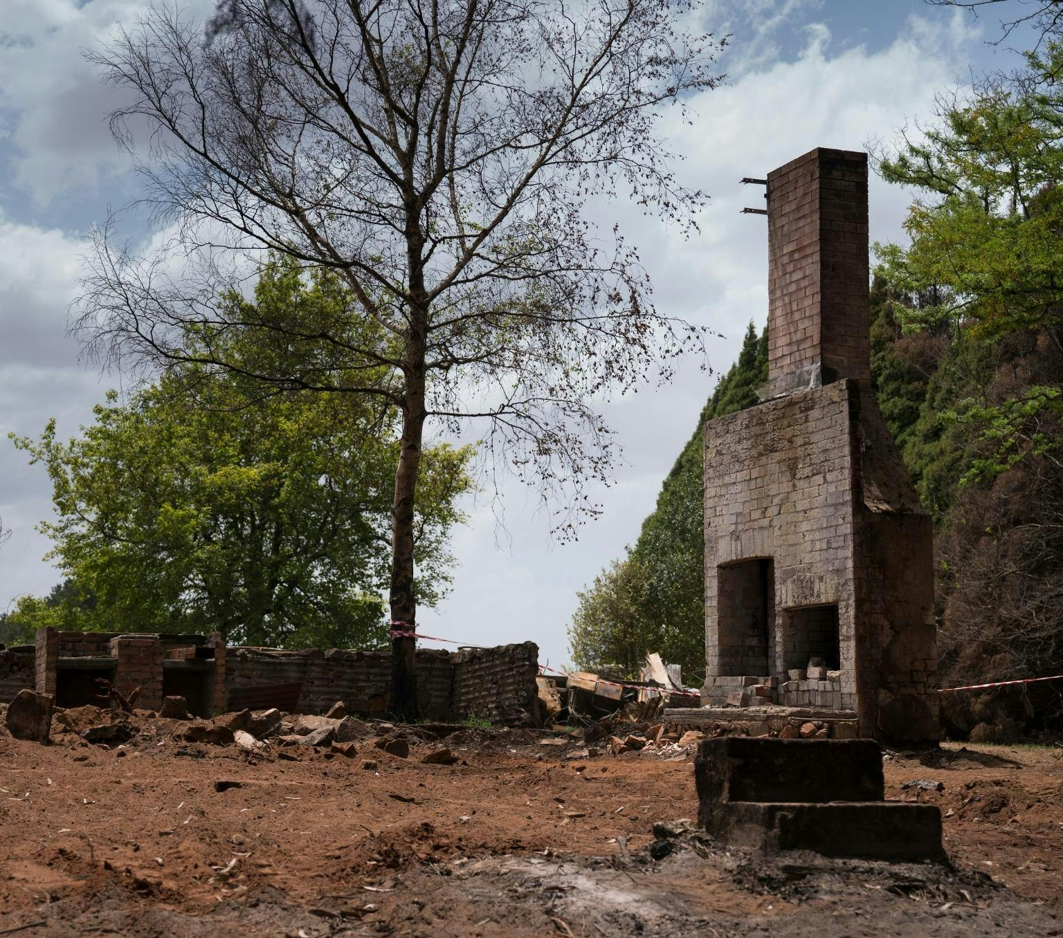 bricks are scattered outside and the chimney of a house remains standing in front of bushland