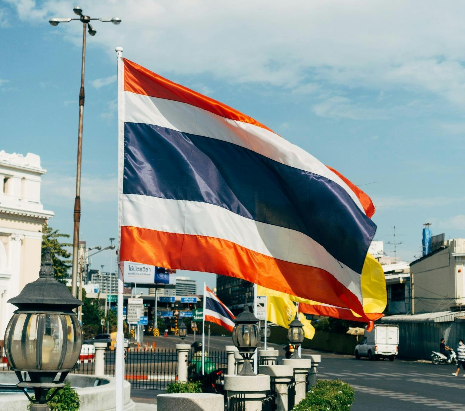 Thai flag which has red white and blue stripes is pictured on a flag pole in front of a city street