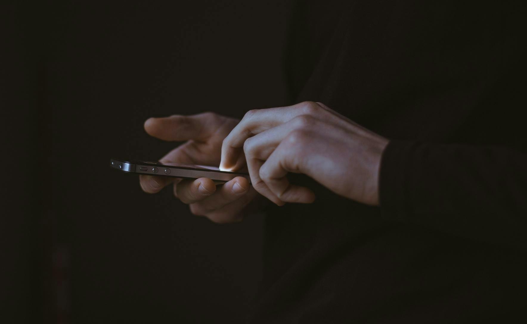 black backrgound with a close up of a person's hands holding a mobile phone