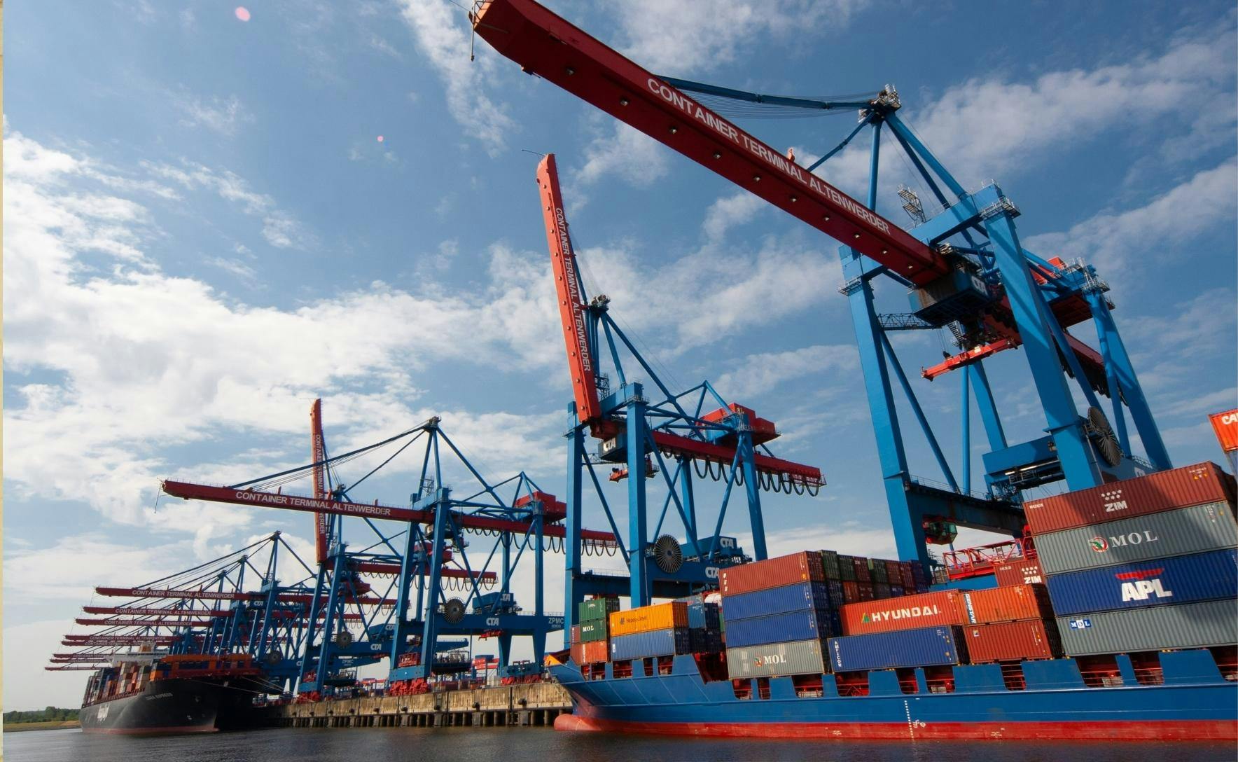 shipping dock with two large shipping boats filled with red and blue shipping containers and cranes looming above