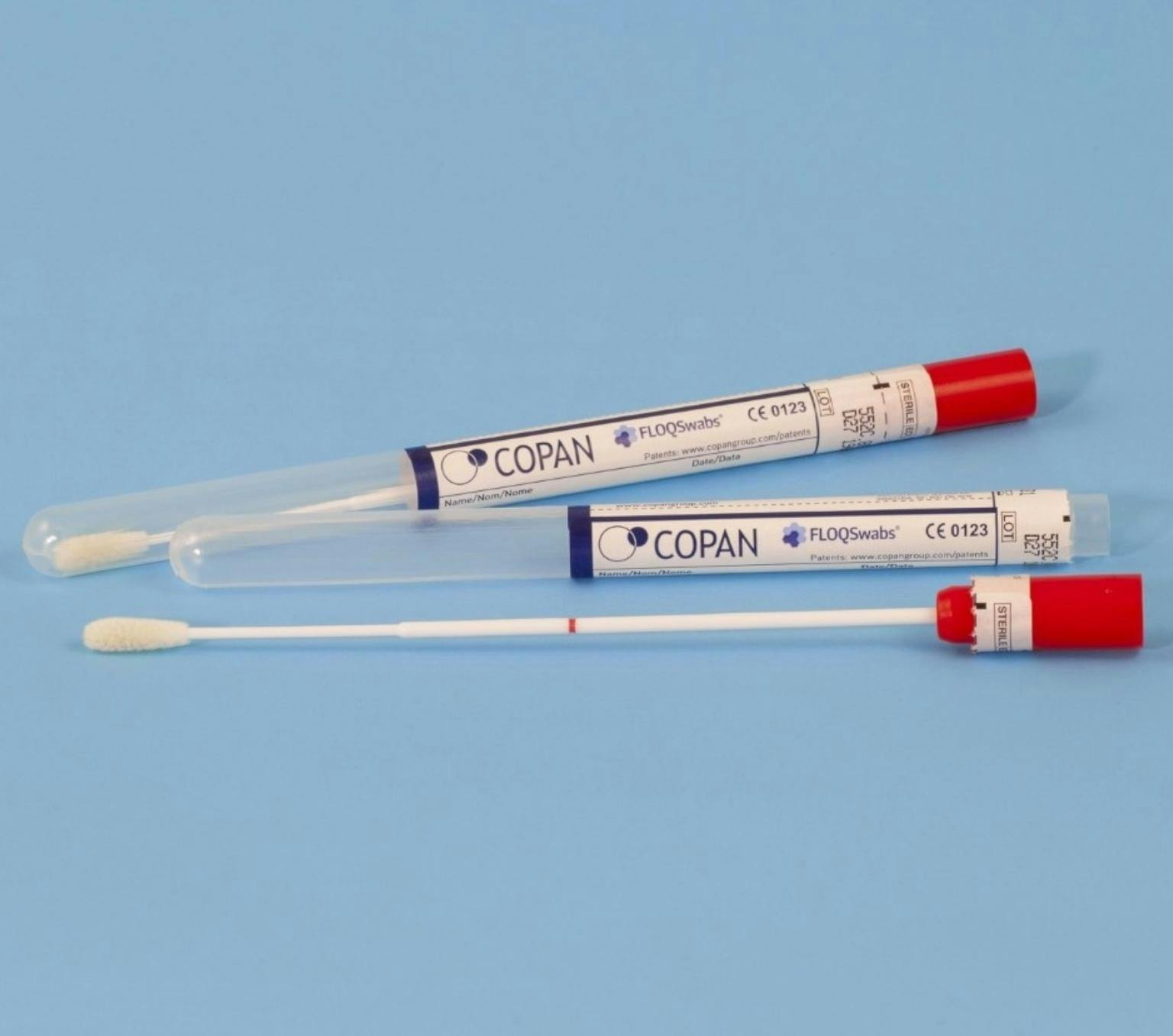 Blue background with to self-testing swab kits. The kits have a clear plastic tube with a label reading COPAN. The long white collection swab has a red lid.