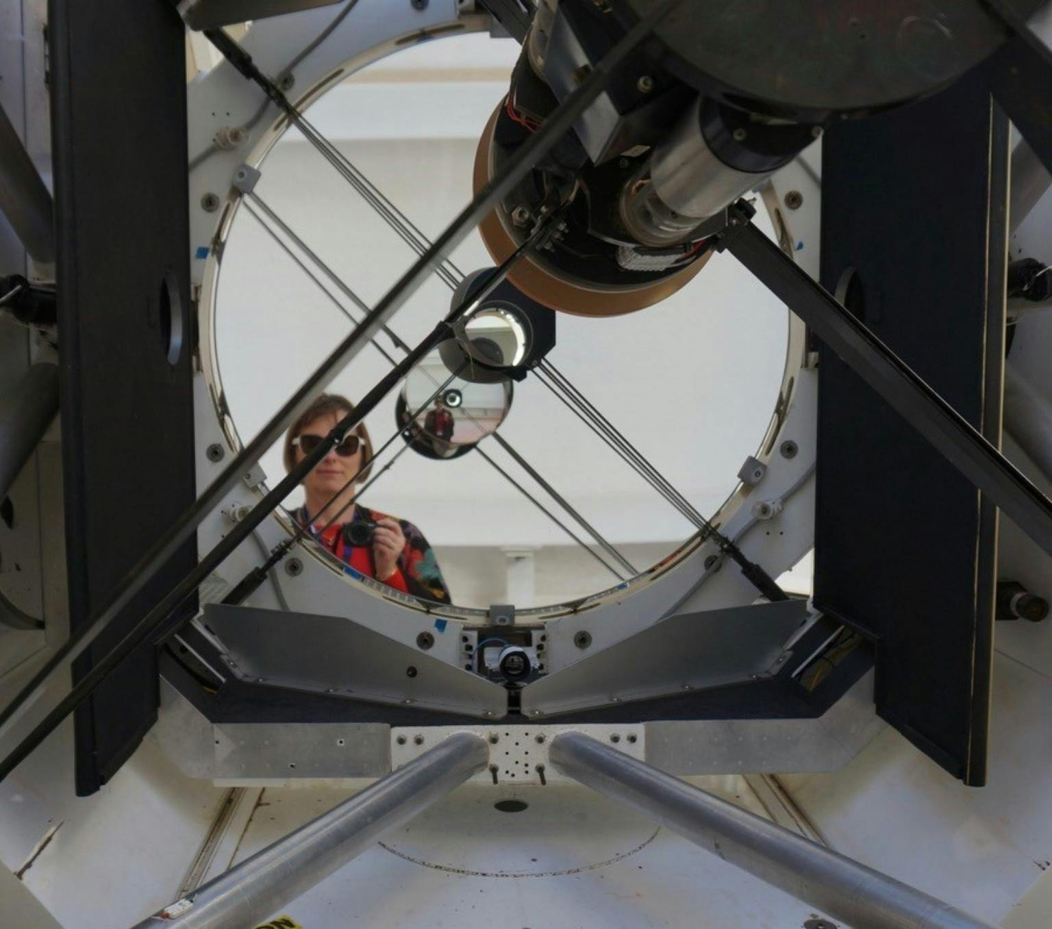 Celine is pictured wearing sunglasses. She is standing behind the EOS 1.8 meter telescope with has a wide circular hole and long metal beams