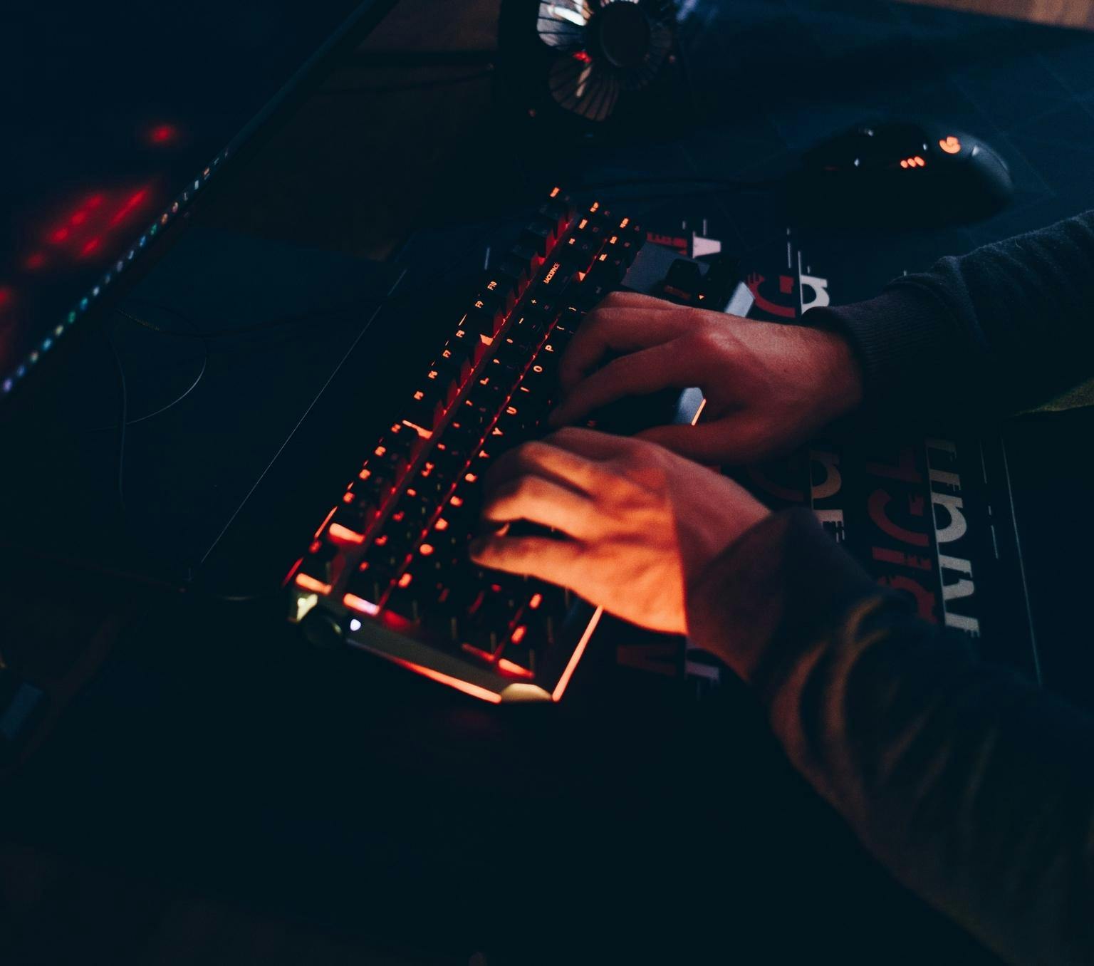 close-up of a persons hands typing on a keyboard. The keyboard is lit by red lights.