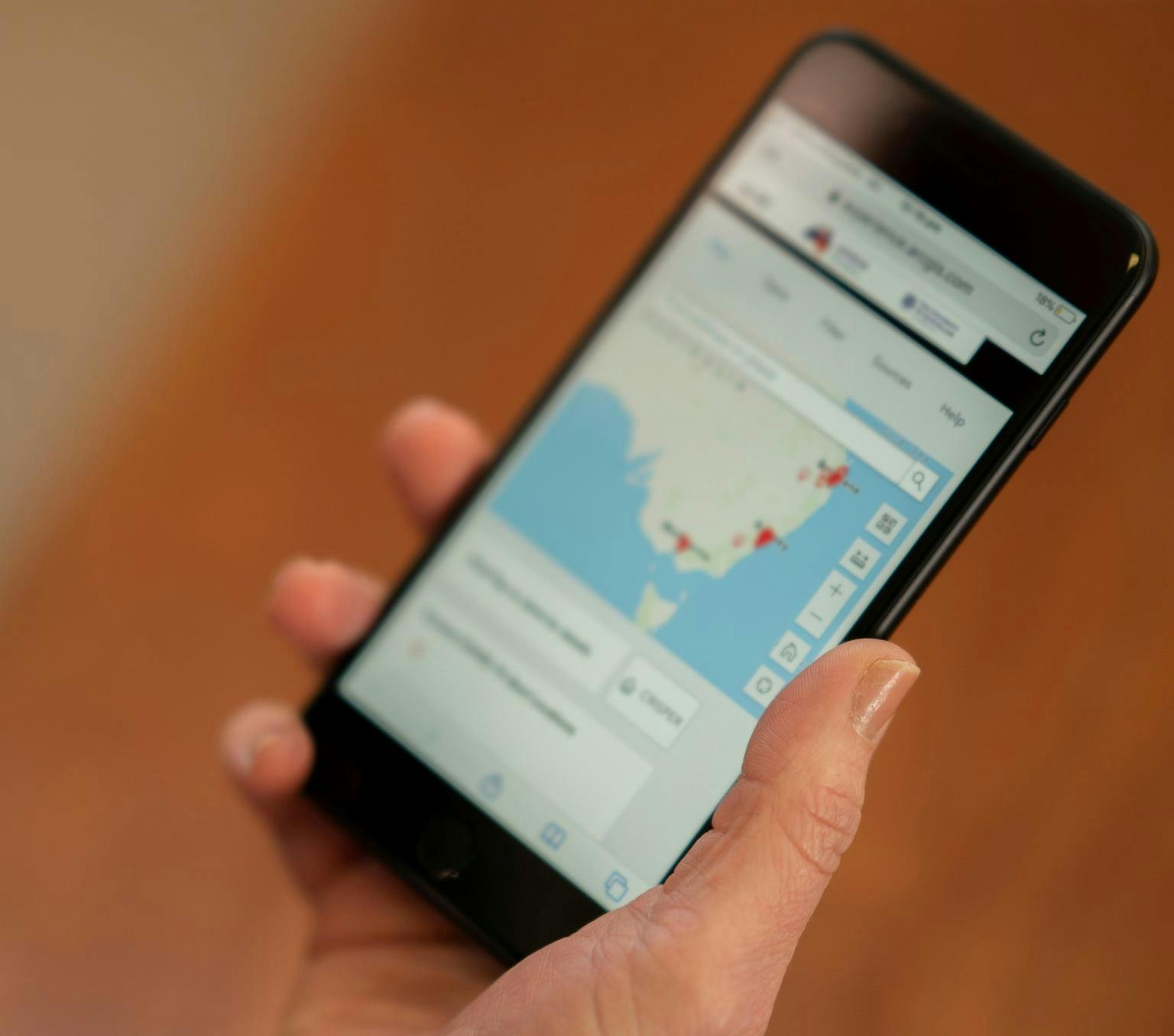 A mobile phone showing a map of Australia with red dots in some locations is held in a the hands of an unidentified person.