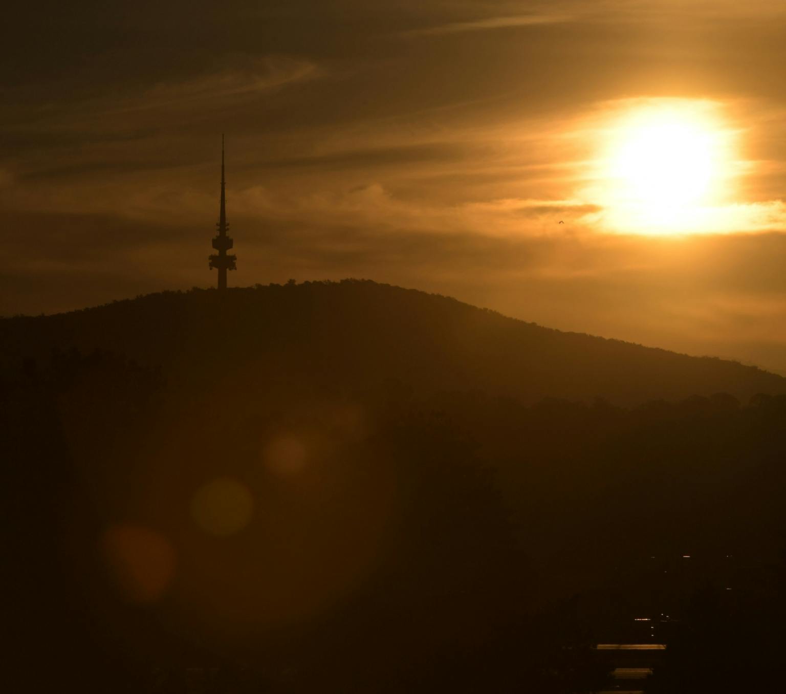 Orange sky with a bright sun in the top right corner illuminates a mountain with a telecommunications tower on its peak